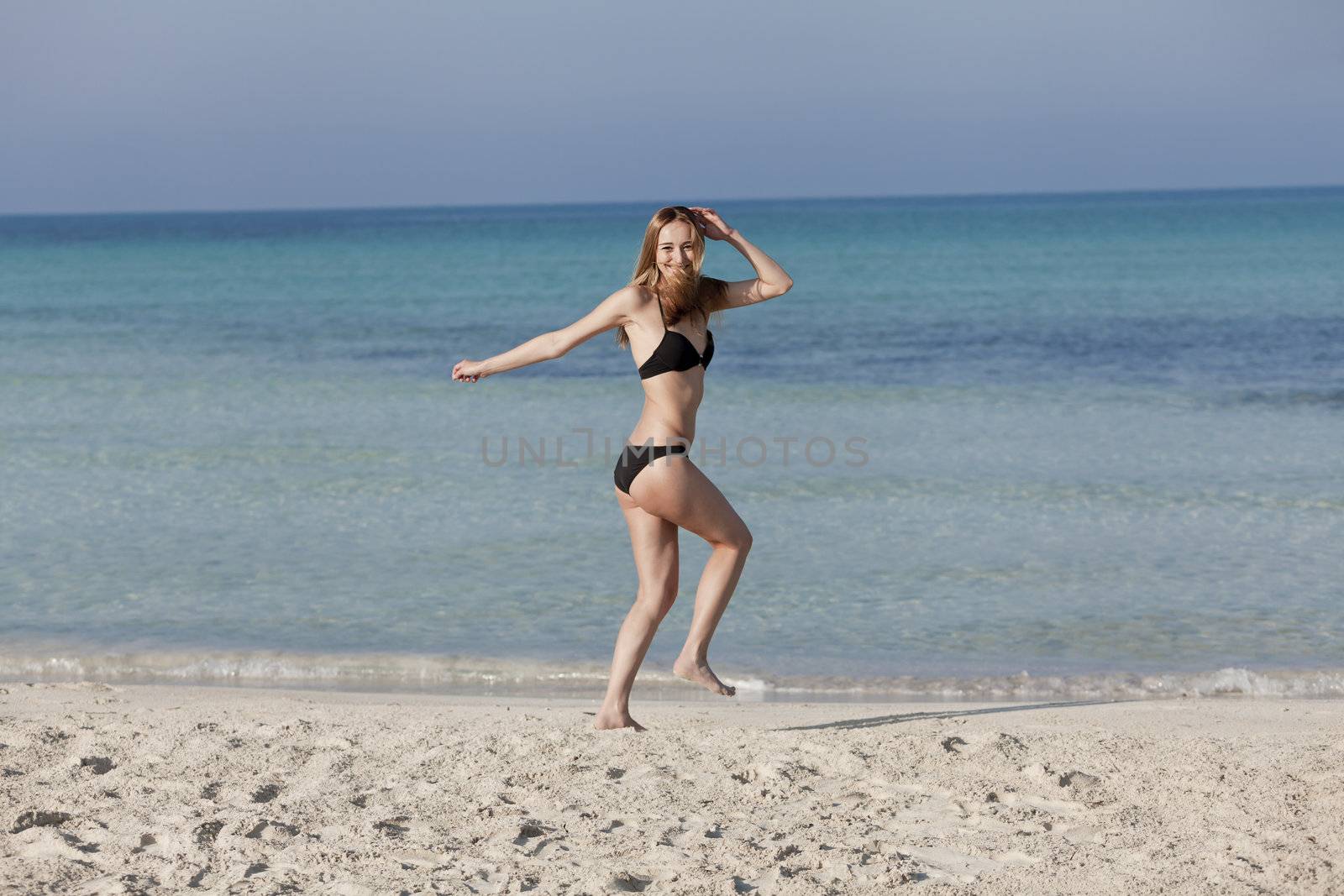 Young woman with black bikini girl on the beach in the sea jumping in the summer holidays