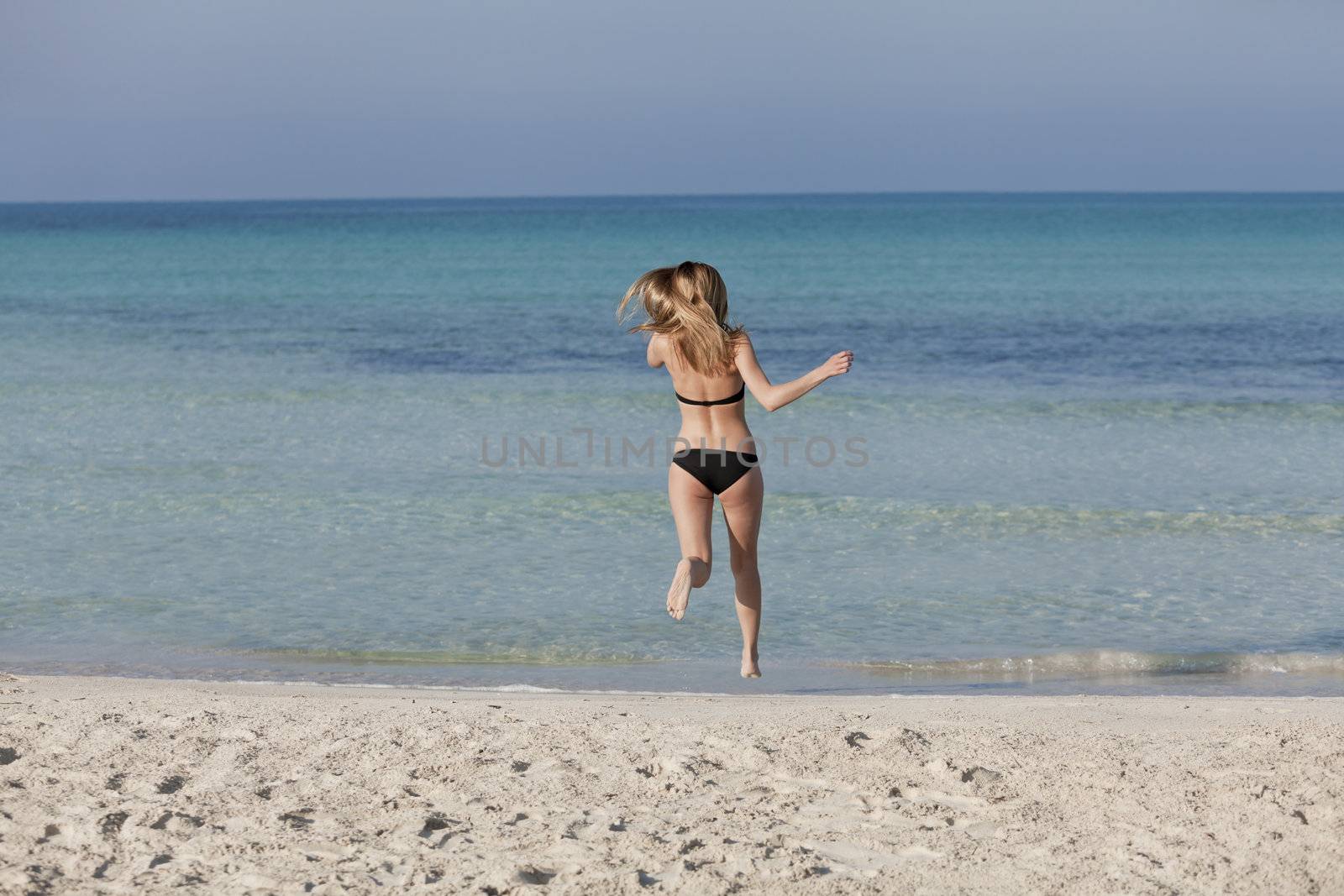 Young woman with black bikini girl on the beach in the sea jumping in the summer holidays