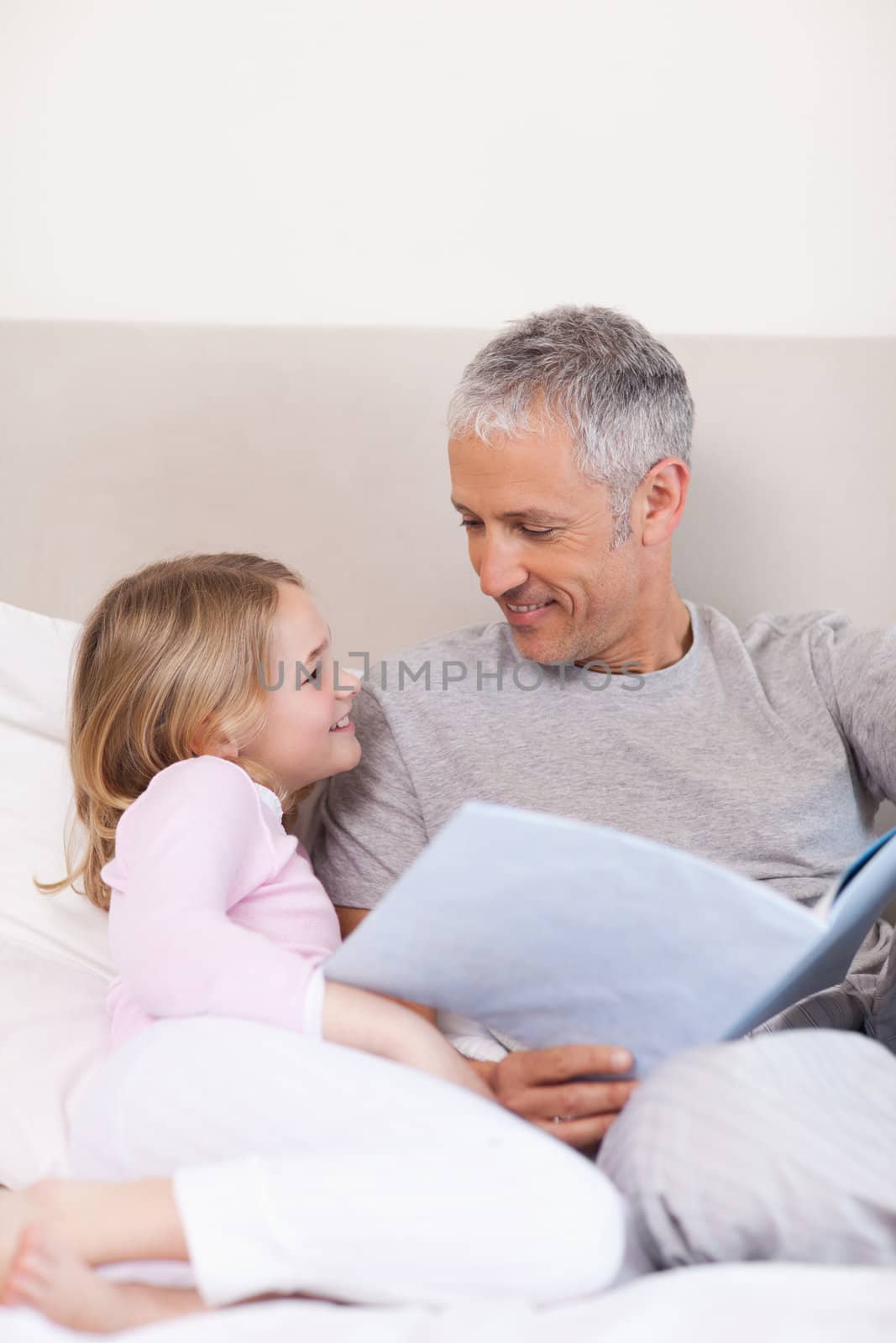 Portrait of a smiling father reading a story to his daughter in a bedroom