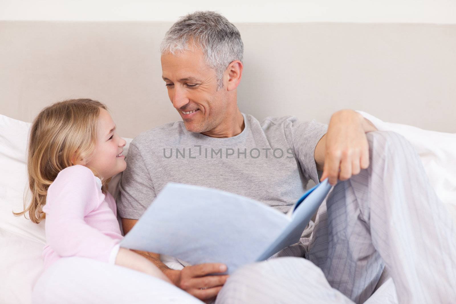 Happy father reading a story to his daughter in a bedroom
