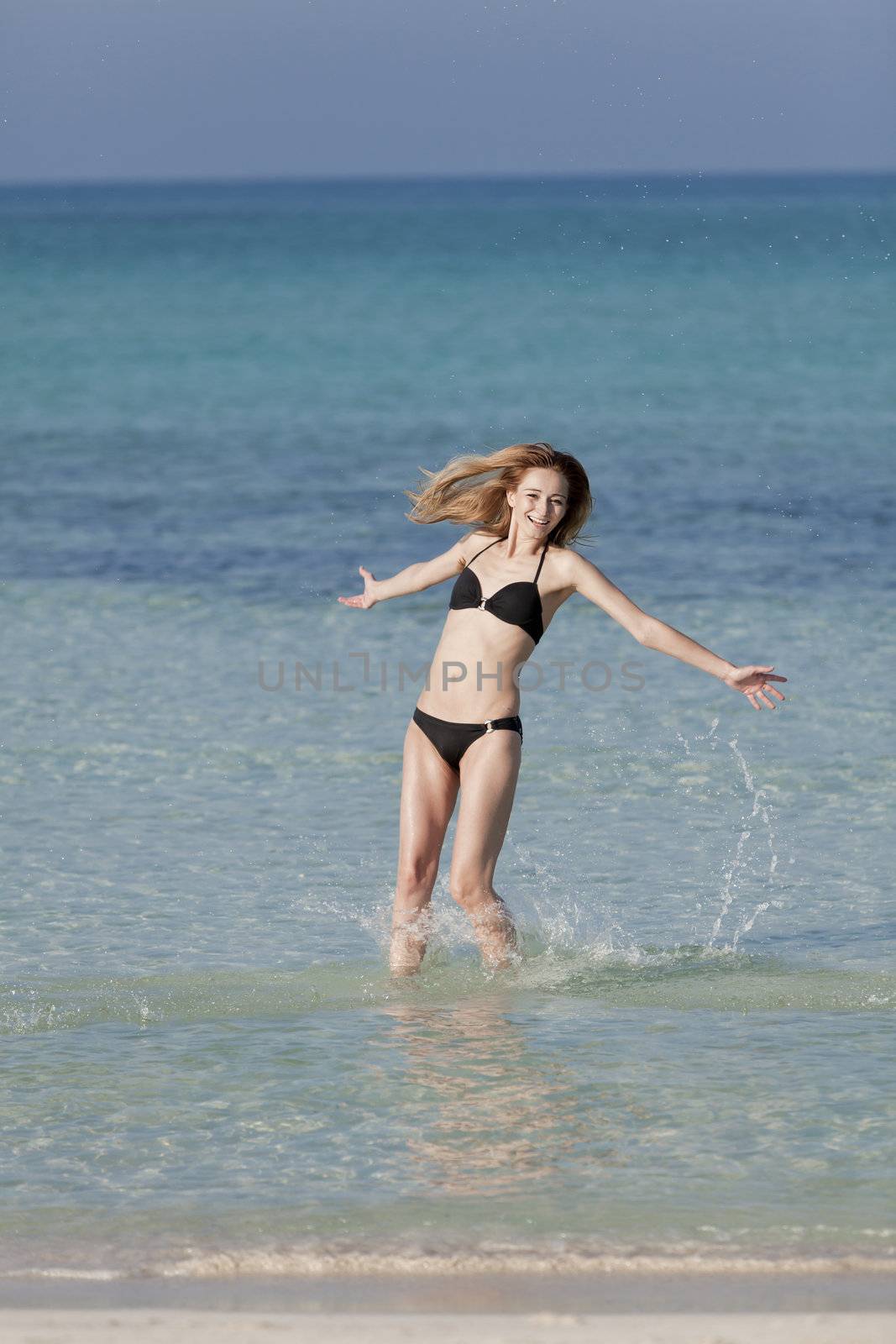 Girl young woman jumping in the water at the beach jumping happily in the sea in summer vacation