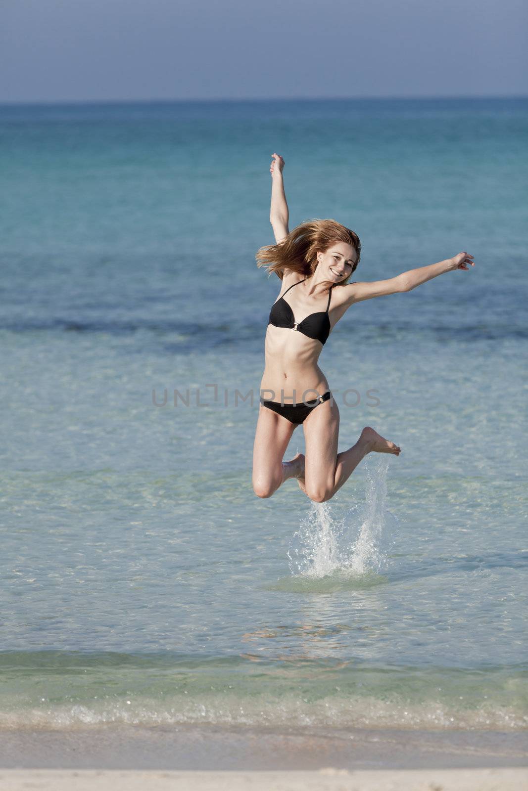 Girl young woman jumping in the water at the beach jumping happily in the sea in summer vacation
