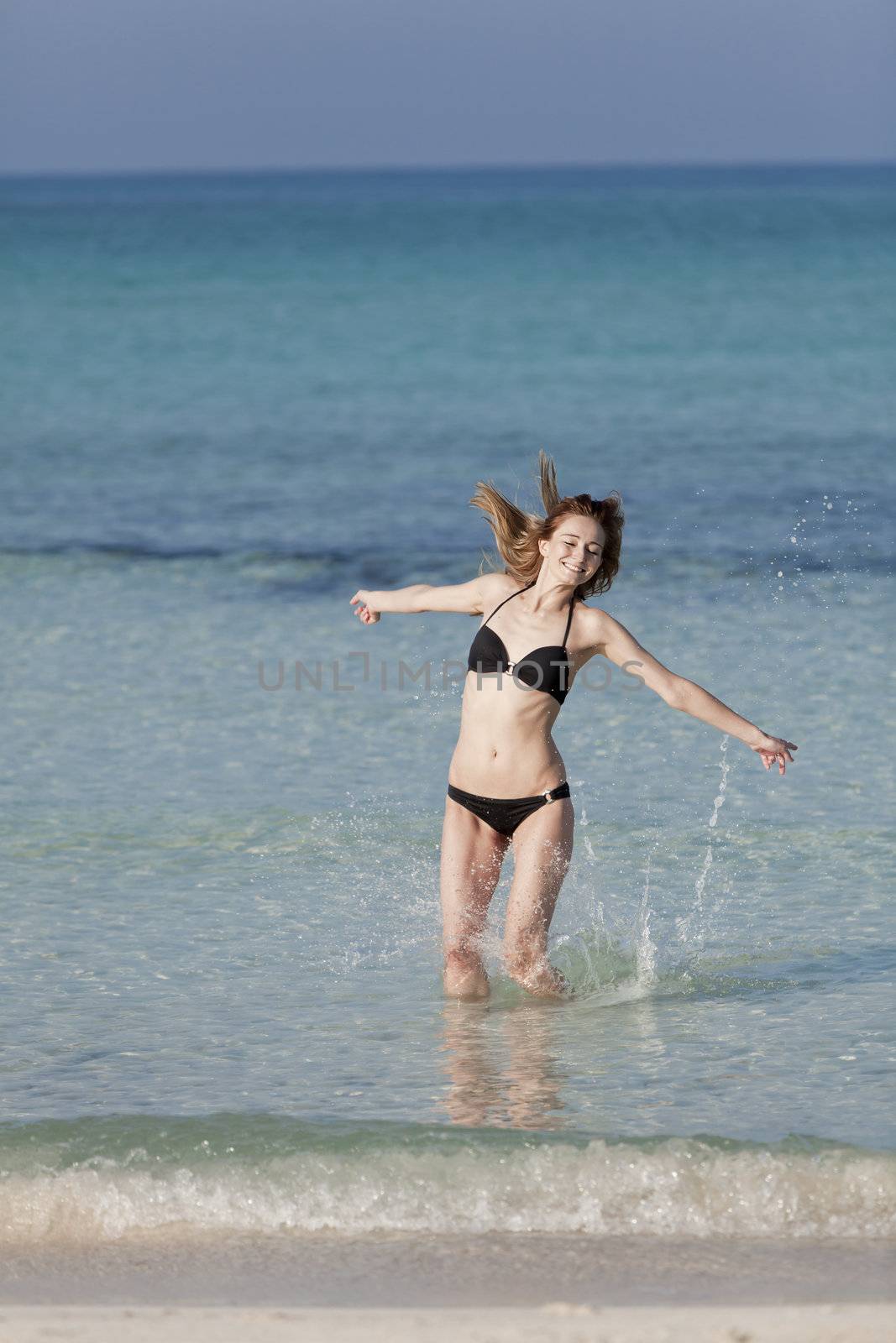Girl young woman jumping in the water at the beach jumping happily in the sea in summer vacation