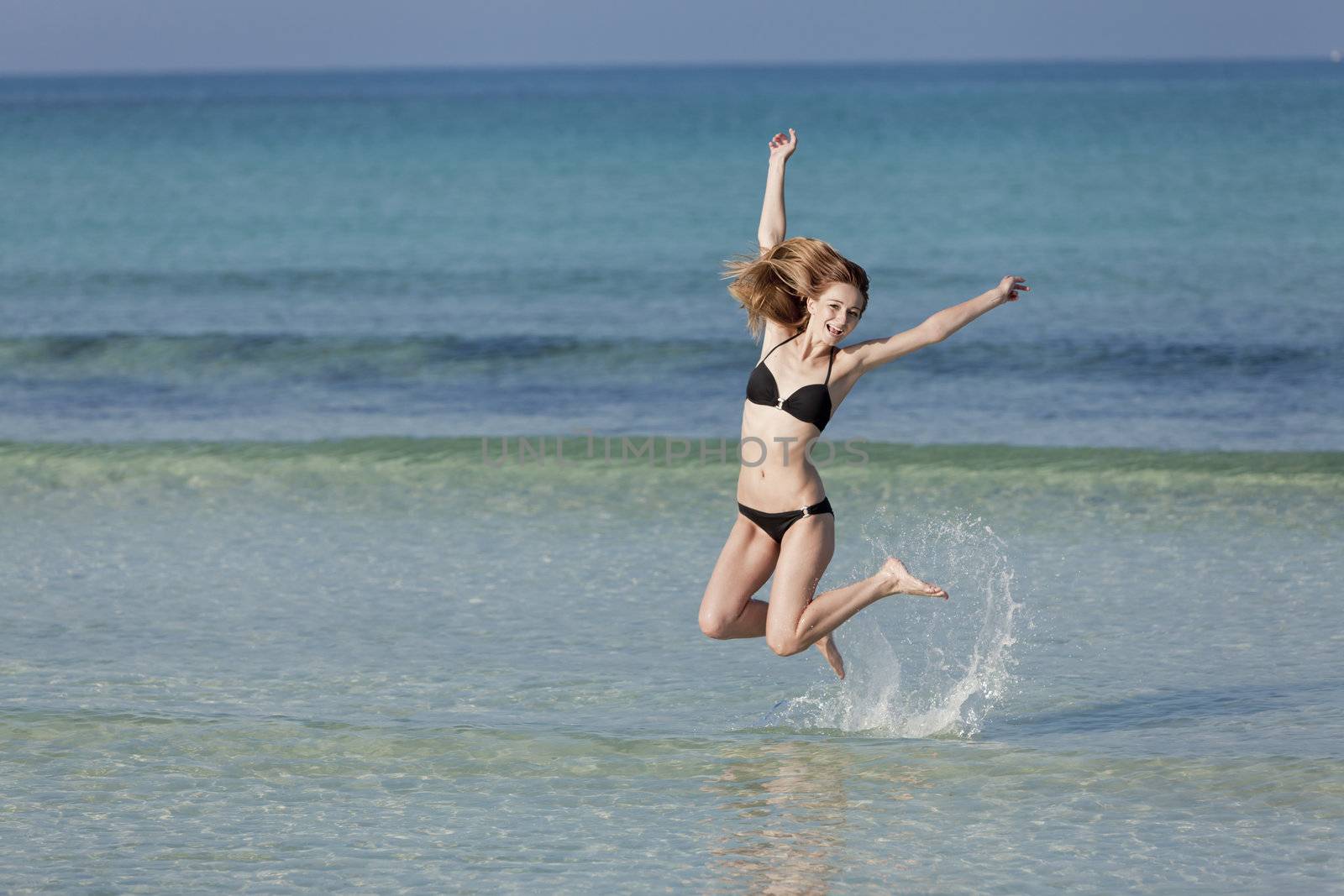 Girl, young woman jumping in the water at the beach jumping happily in the sea in summer vacation