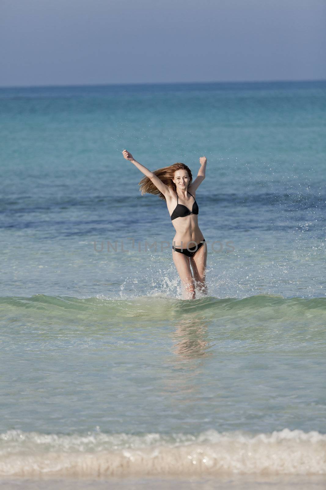 Young woman with black bikini girl on the beach in the sea jumping in the summer holidays