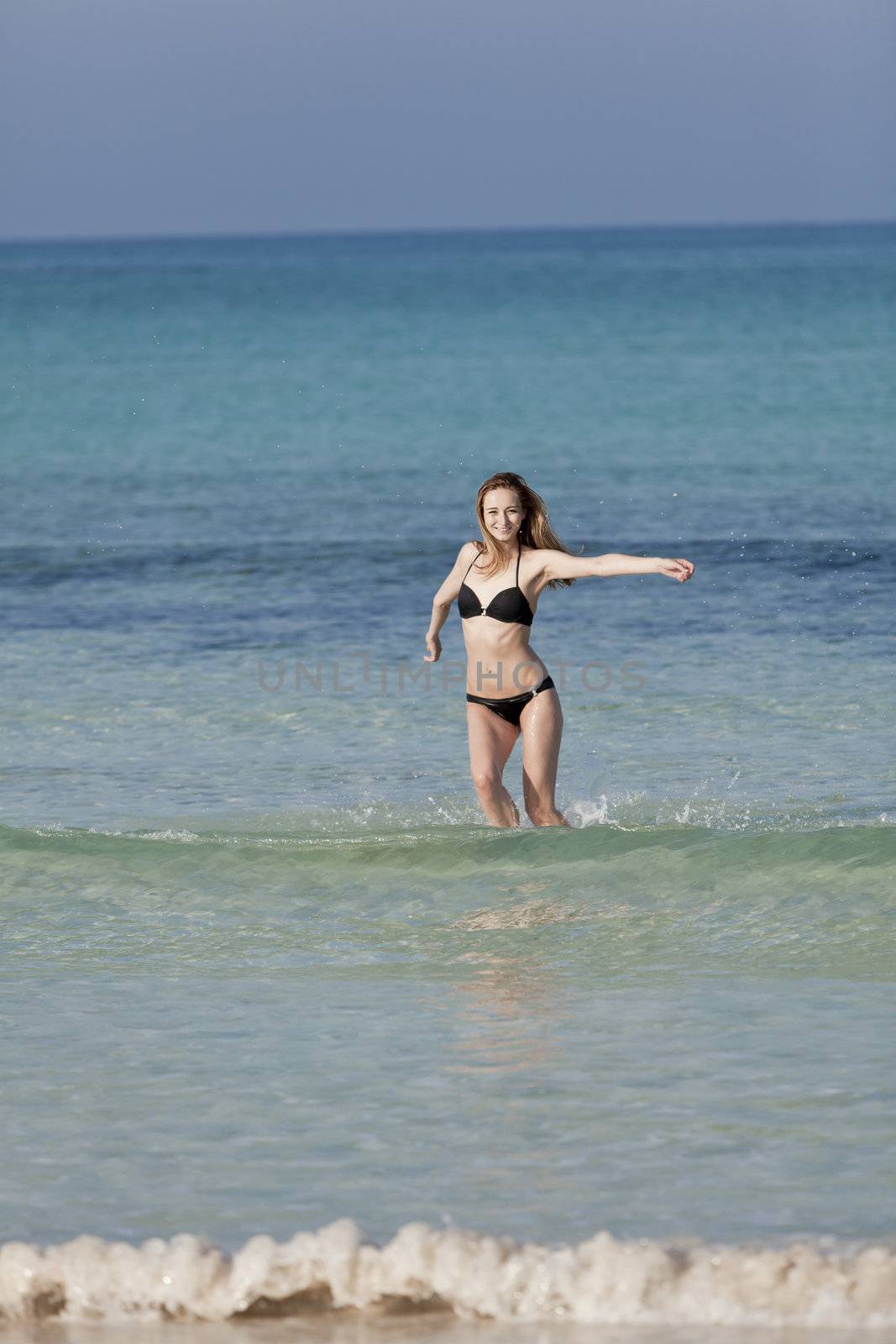Young woman with black bikini girl on the beach in the sea jumping in the summer holidays