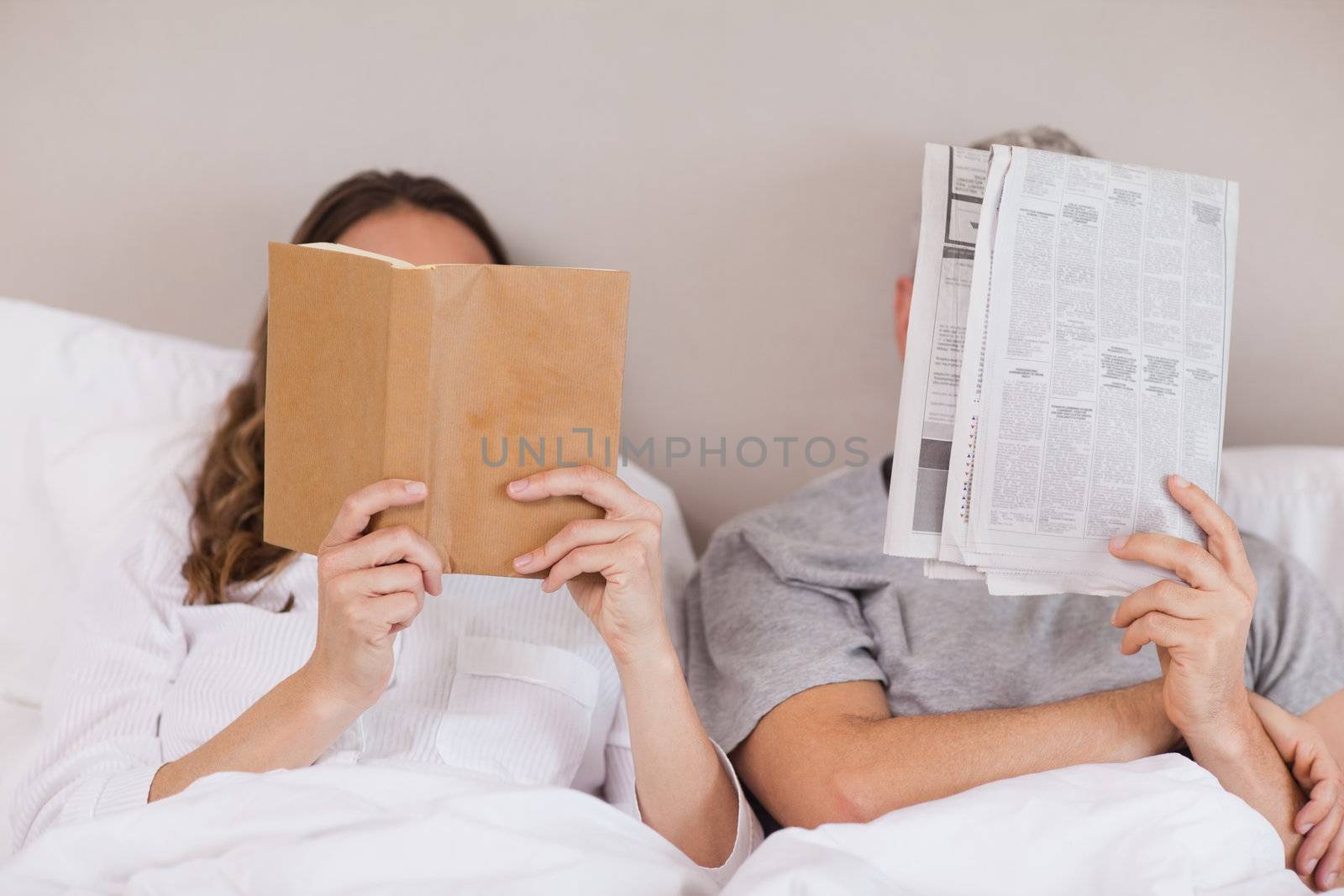 Woman reading a book while her companion is reading a newspaper in their bedroom