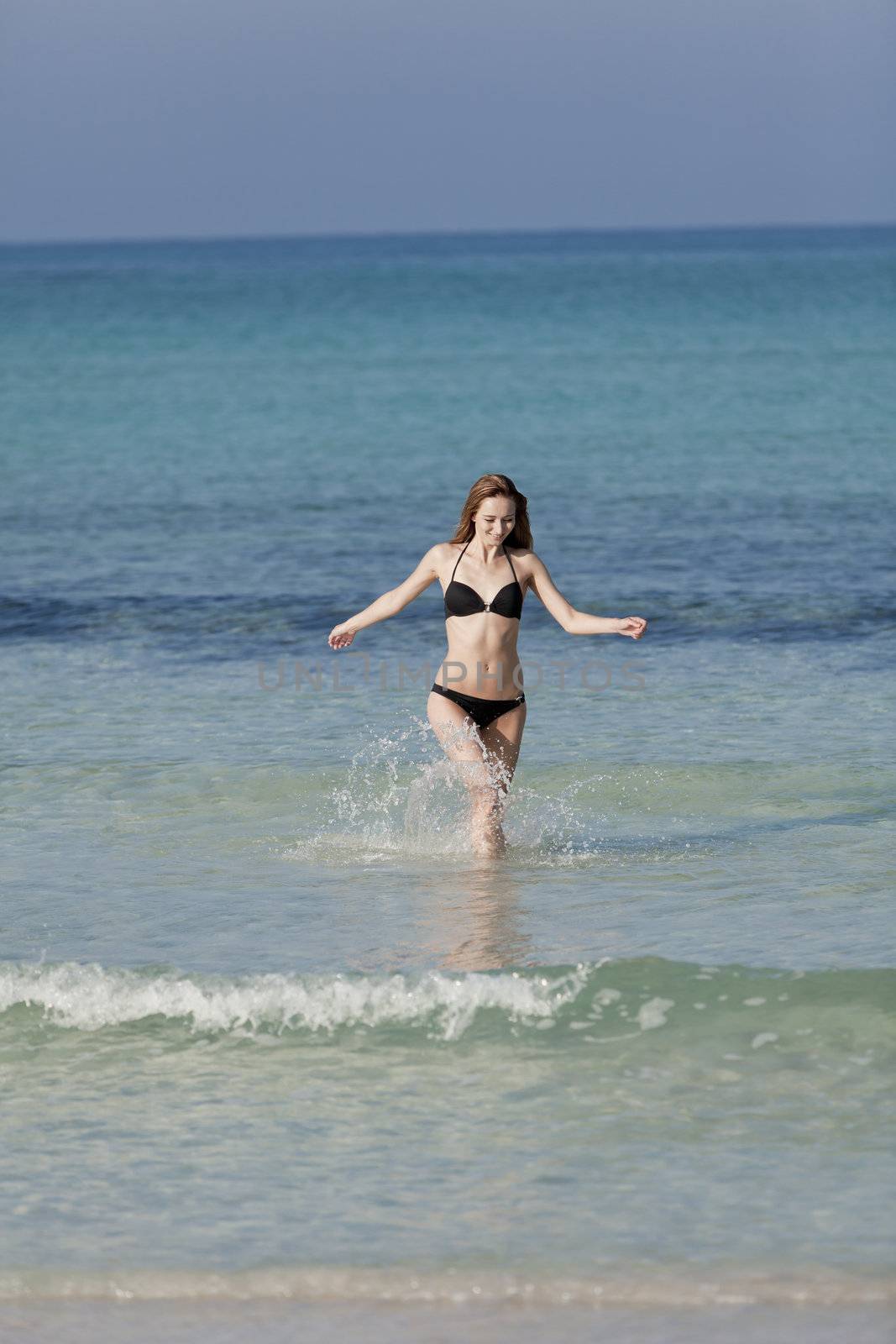 Young woman with black bikini girl on the beach in the sea jumping in the summer holidays