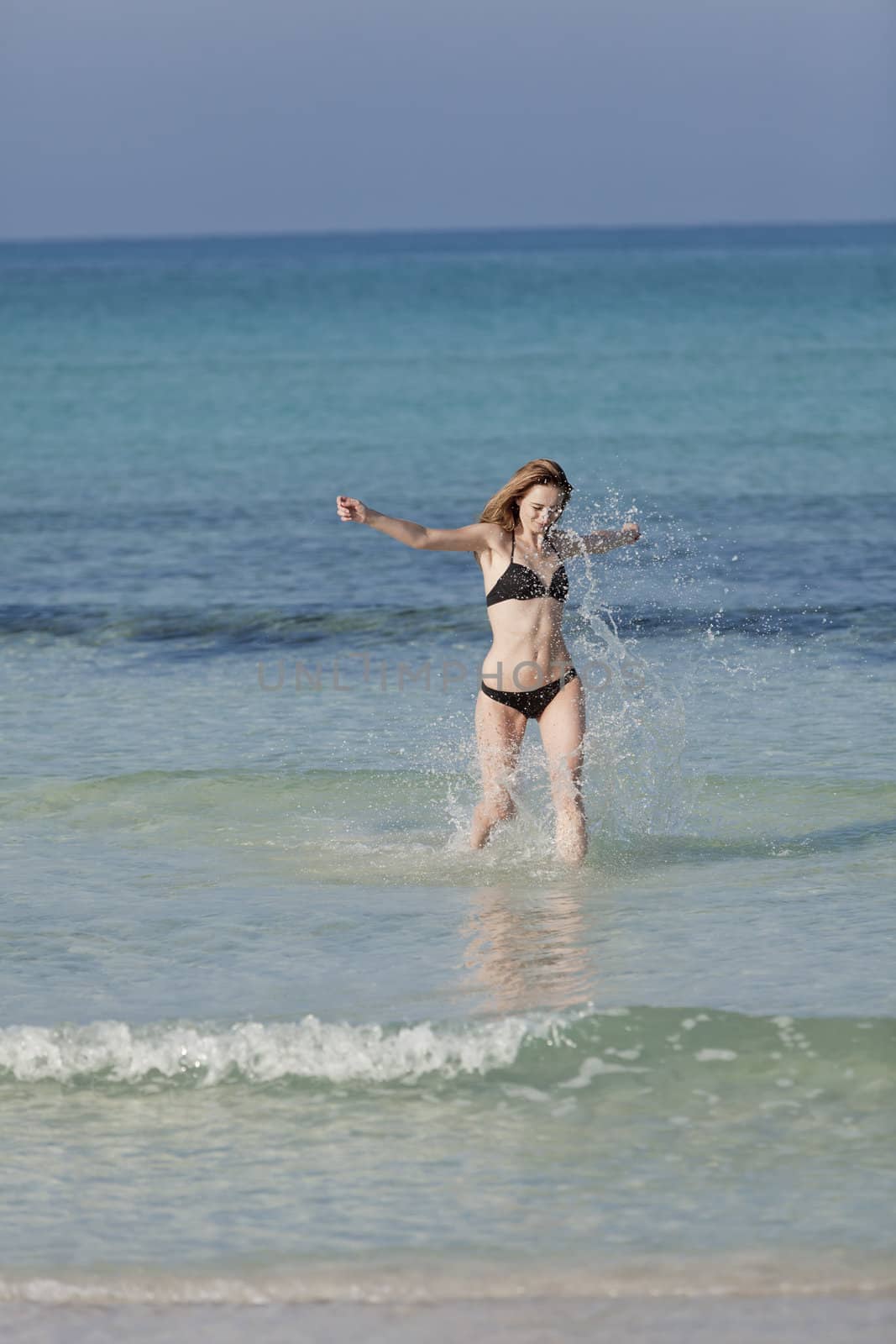 Young woman with black bikini girl on the beach in the sea jumping in the summer holidays