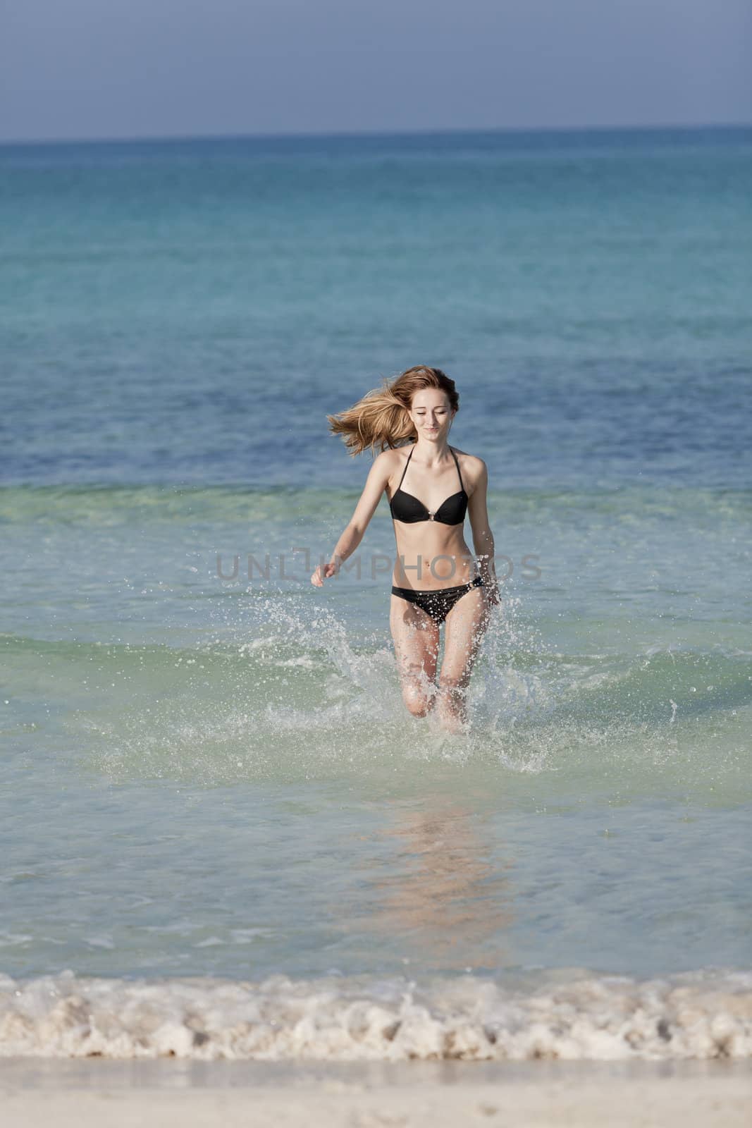 Young woman with black bikini girl on the beach in the sea jumping in the summer holidays