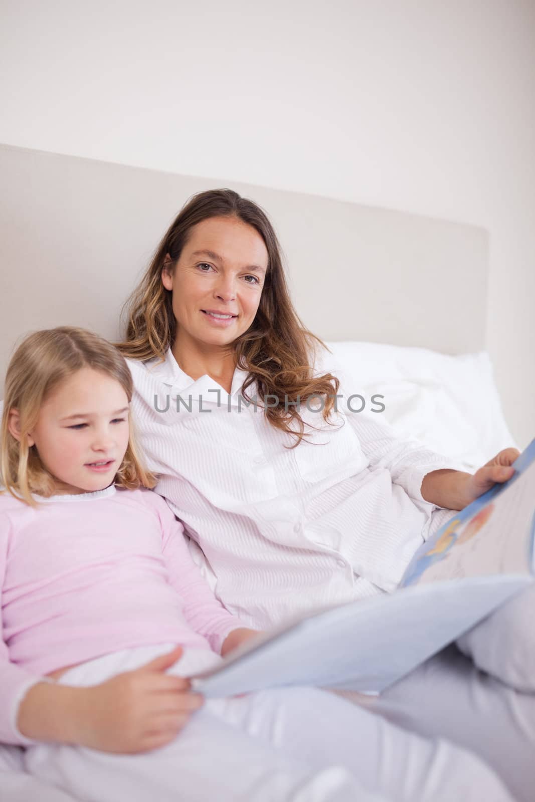 Portrait of a girl reading a book with her mother in a bedroom
