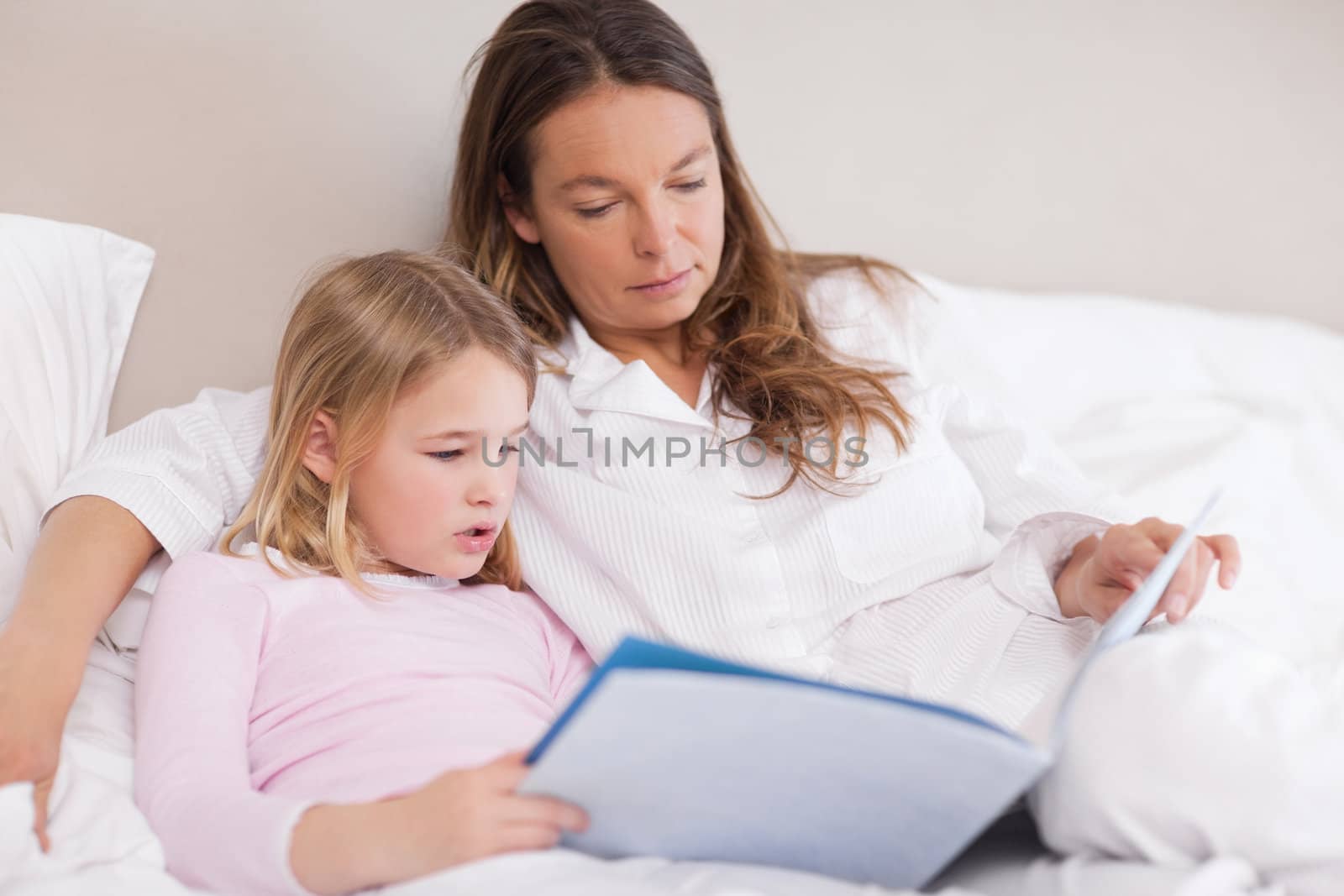 Cute girl reading a book with her mother in a bedroom