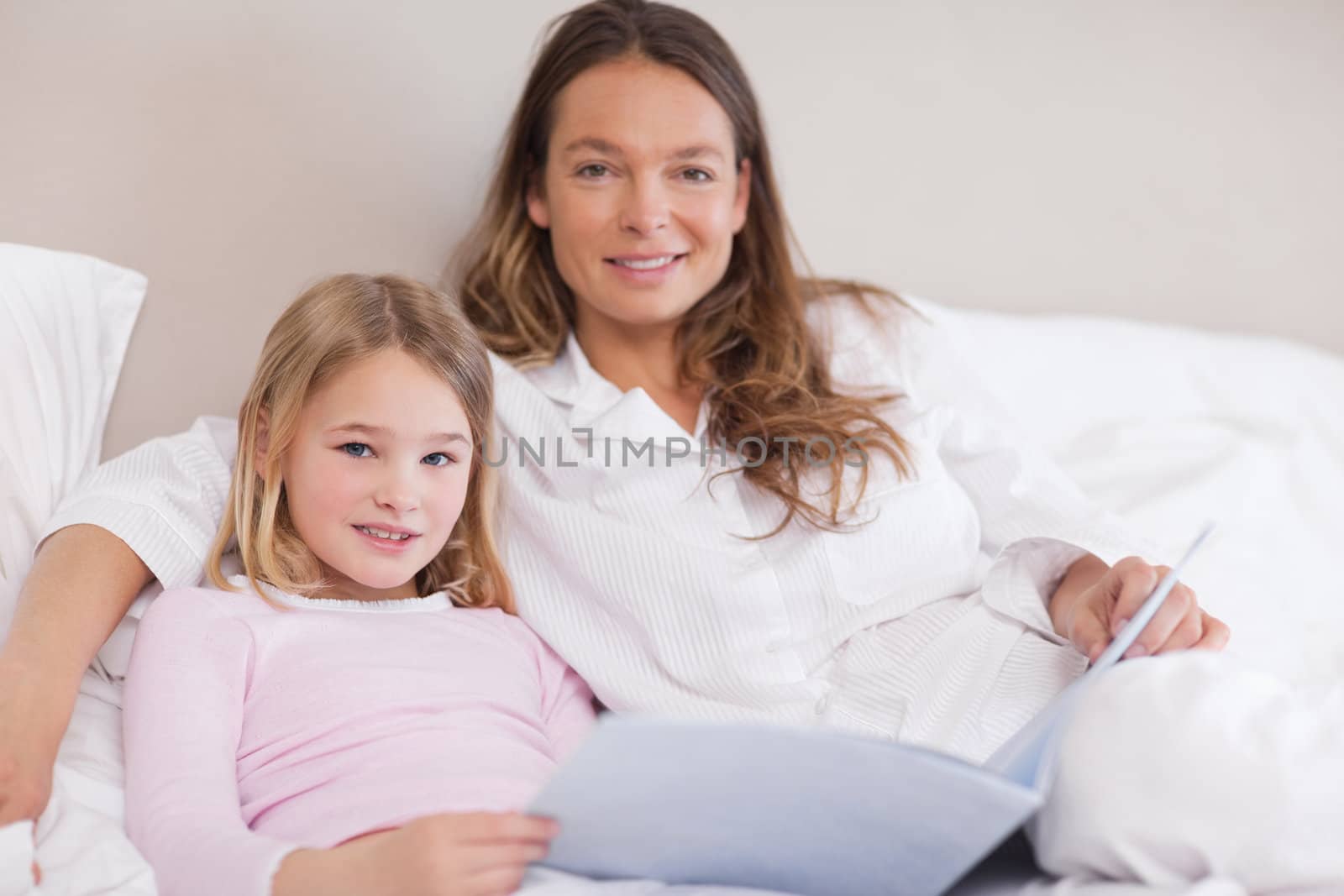 Smiling girl reading a book with her mother in a bedroom