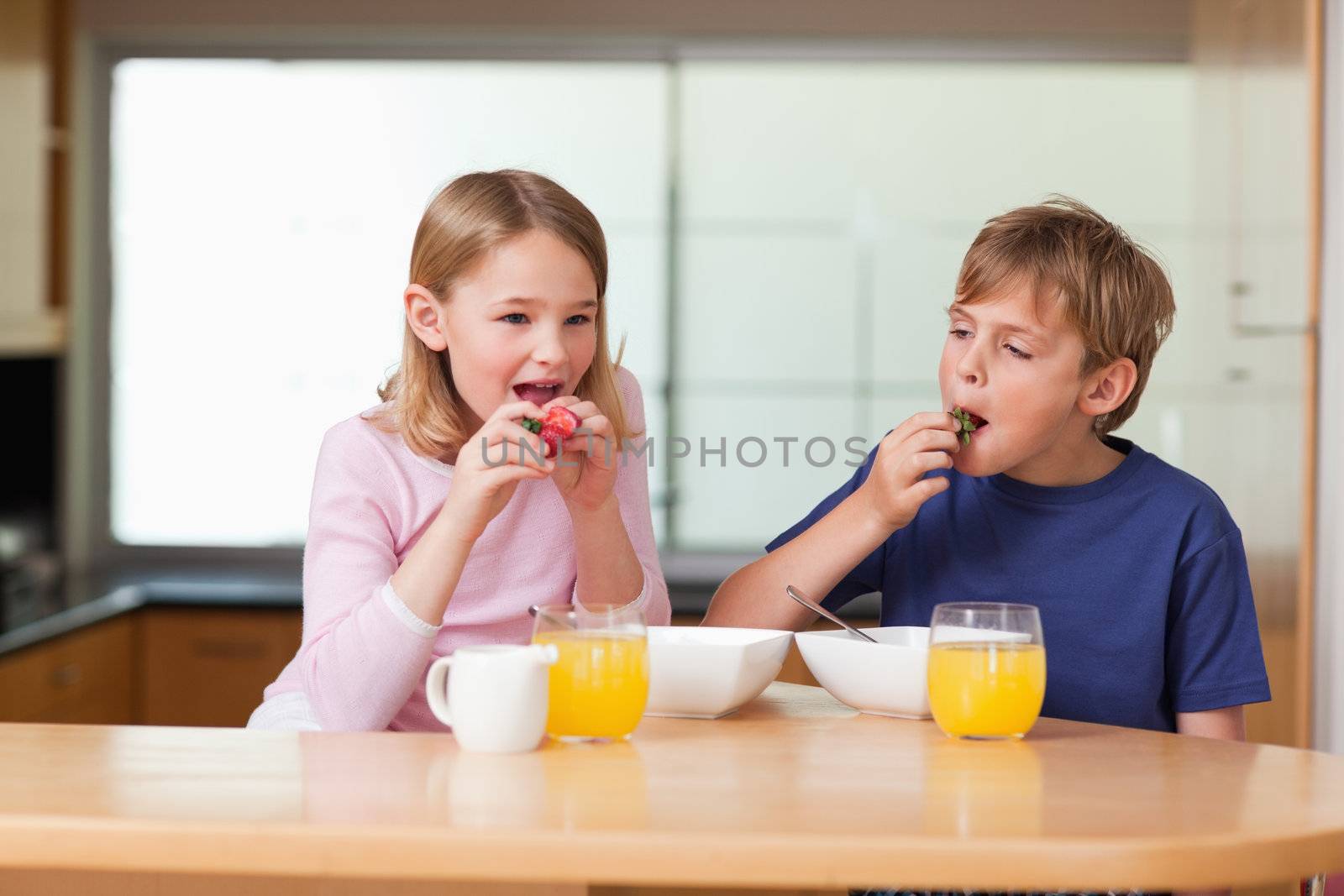 Children eating strawberries for breakfast in a kitchen