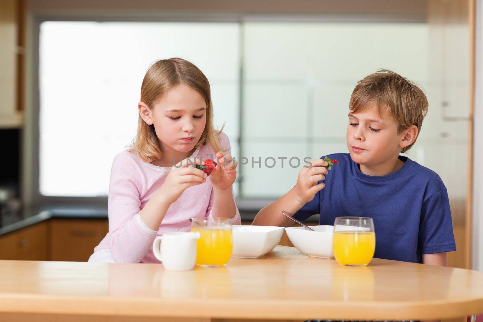 Cute children eating strawberries for breakfast in a kitchen
