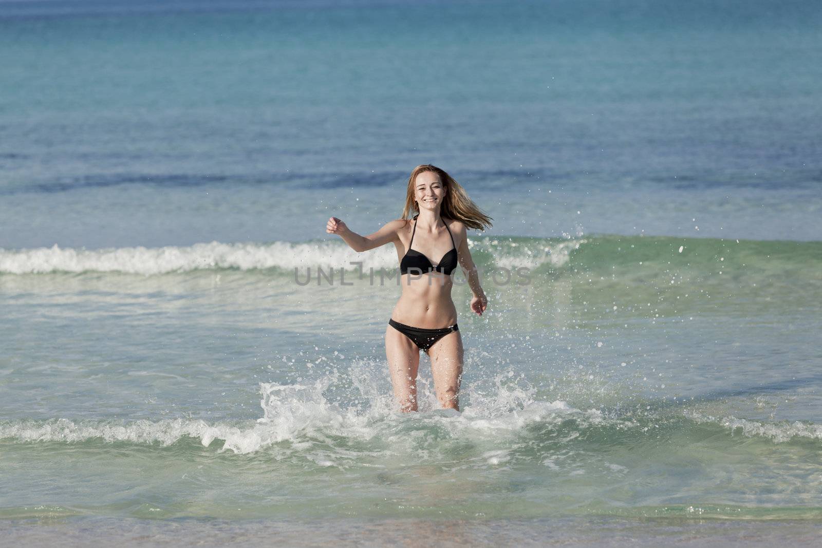 Young woman with black bikini girl on the beach in the sea jumping in the summer holidays