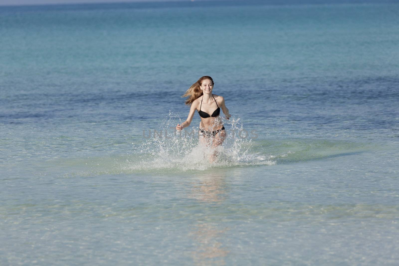 Young woman with black bikini girl on the beach in the sea jumping in the summer holidays