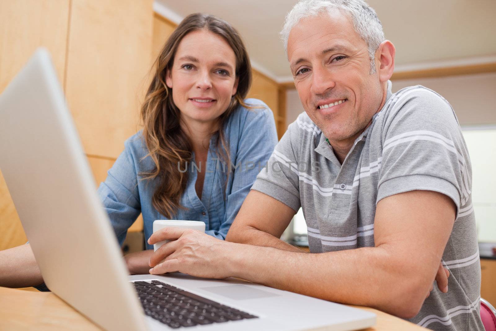 Couple using a laptop while having tea in their kitchen