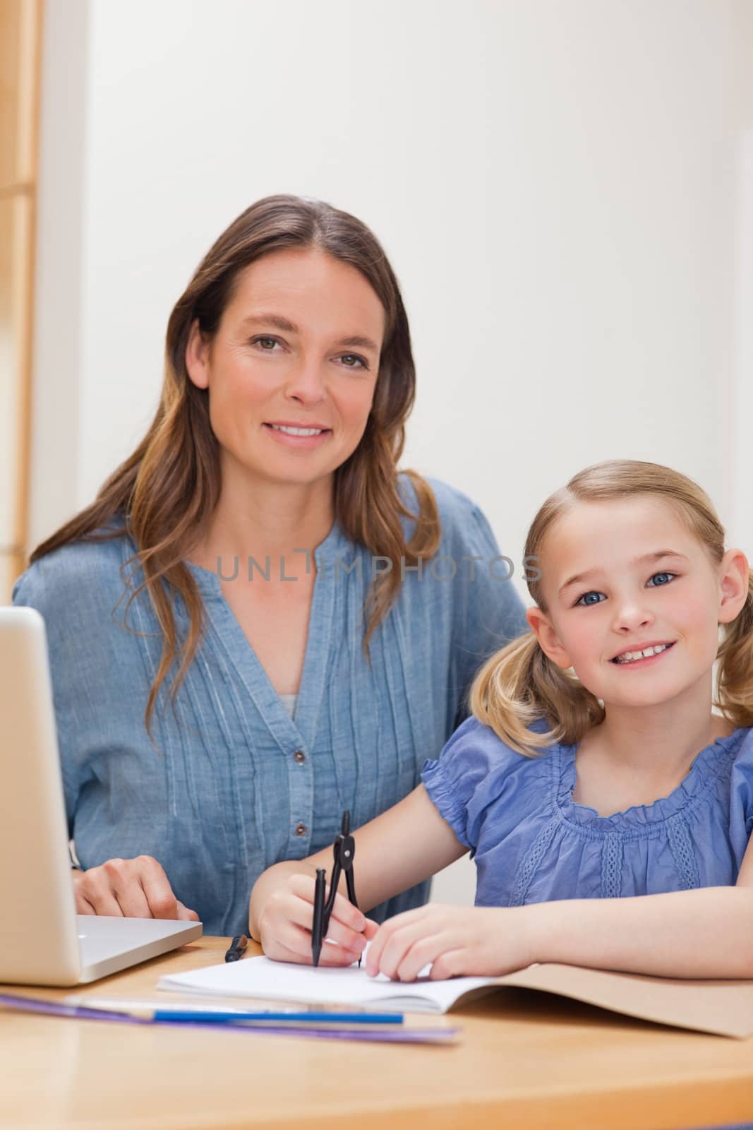 Portrait of a beautiful woman helping her daughter doing her homework in a kitchen