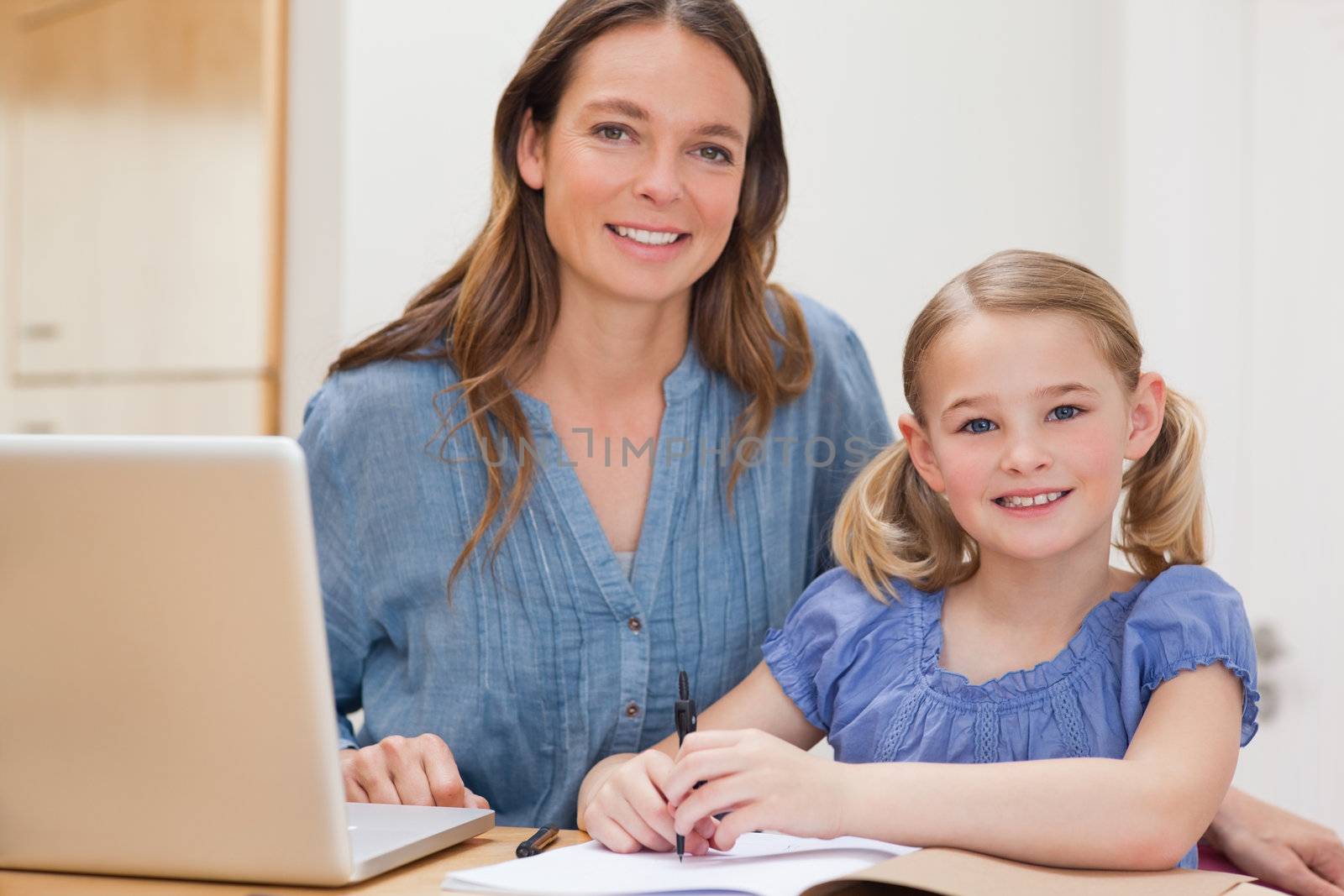 Beautiful woman helping her daughter doing her homework in a kitchen