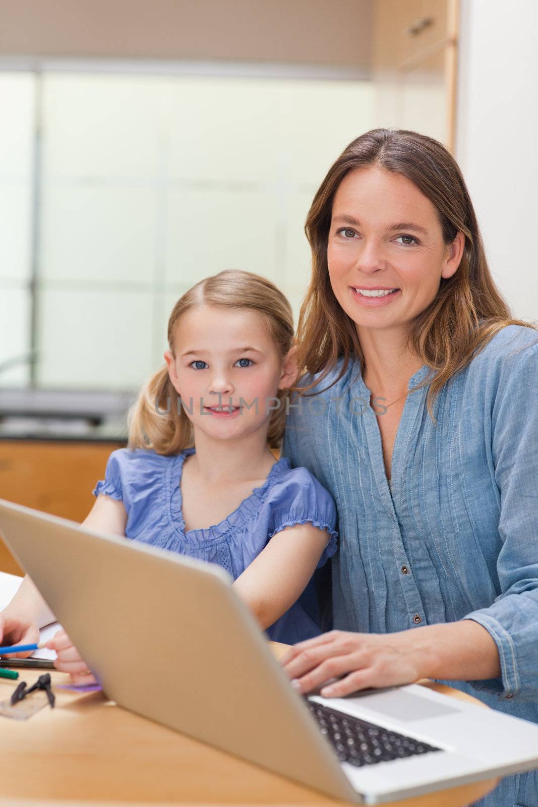 Portrait of a girl doing her homework while her mother is working with laptop in a kitchen