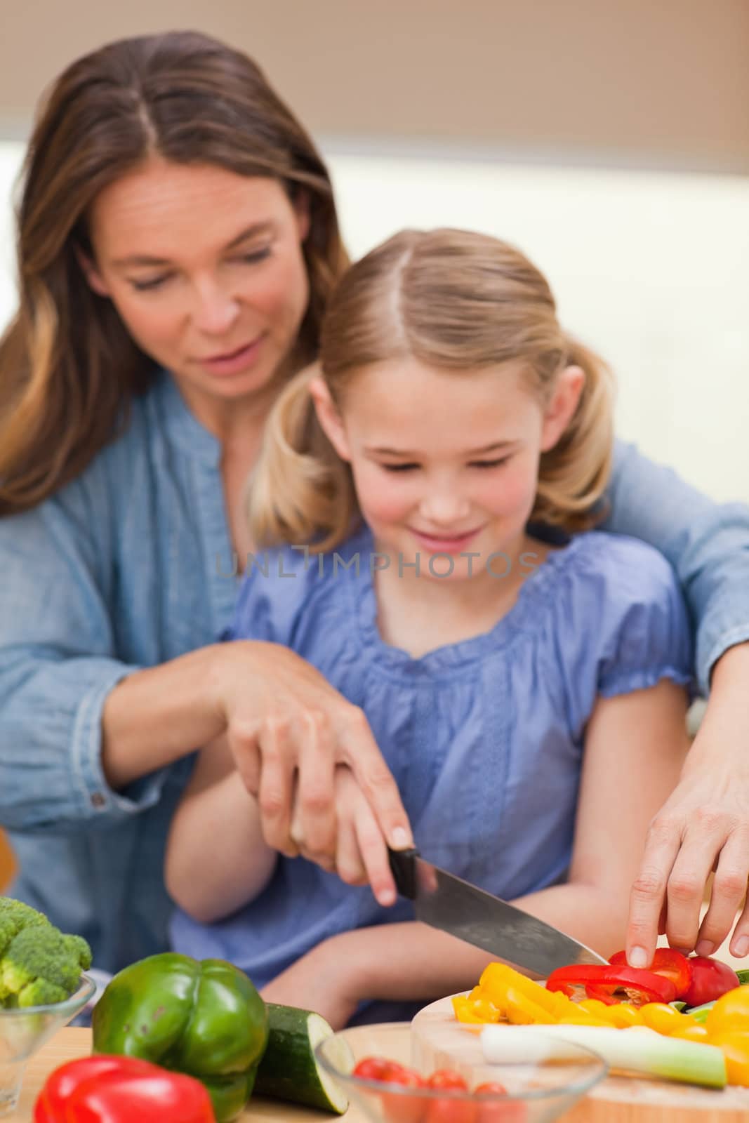 Portrait of a mother slicing pepper with her daughter in a kitchen