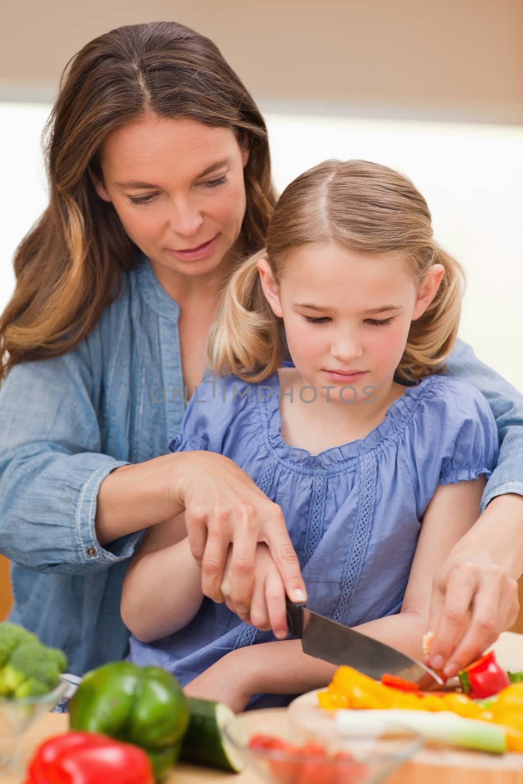 Portrait of a woman slicing pepper with her daughter in a kitchen