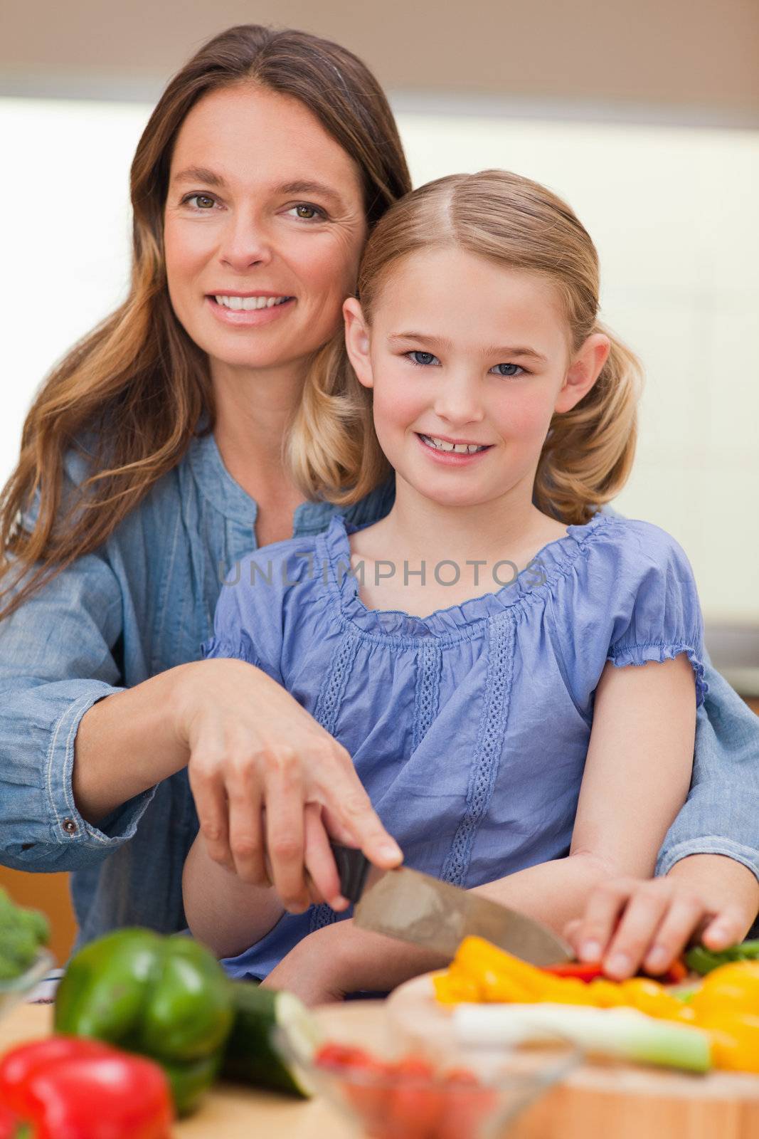 Portrait of a woman slicing bell pepper with her daughter in a kitchen