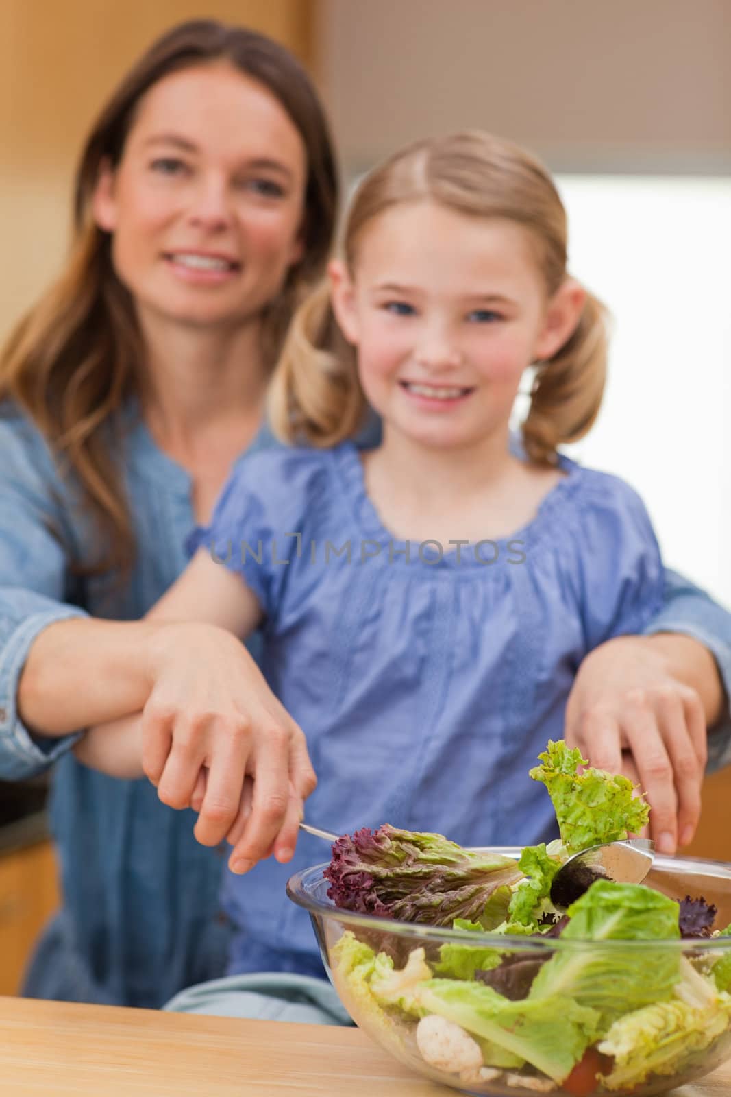 Portrait of a happy woman preparing a salad with her daughter in a kitchen