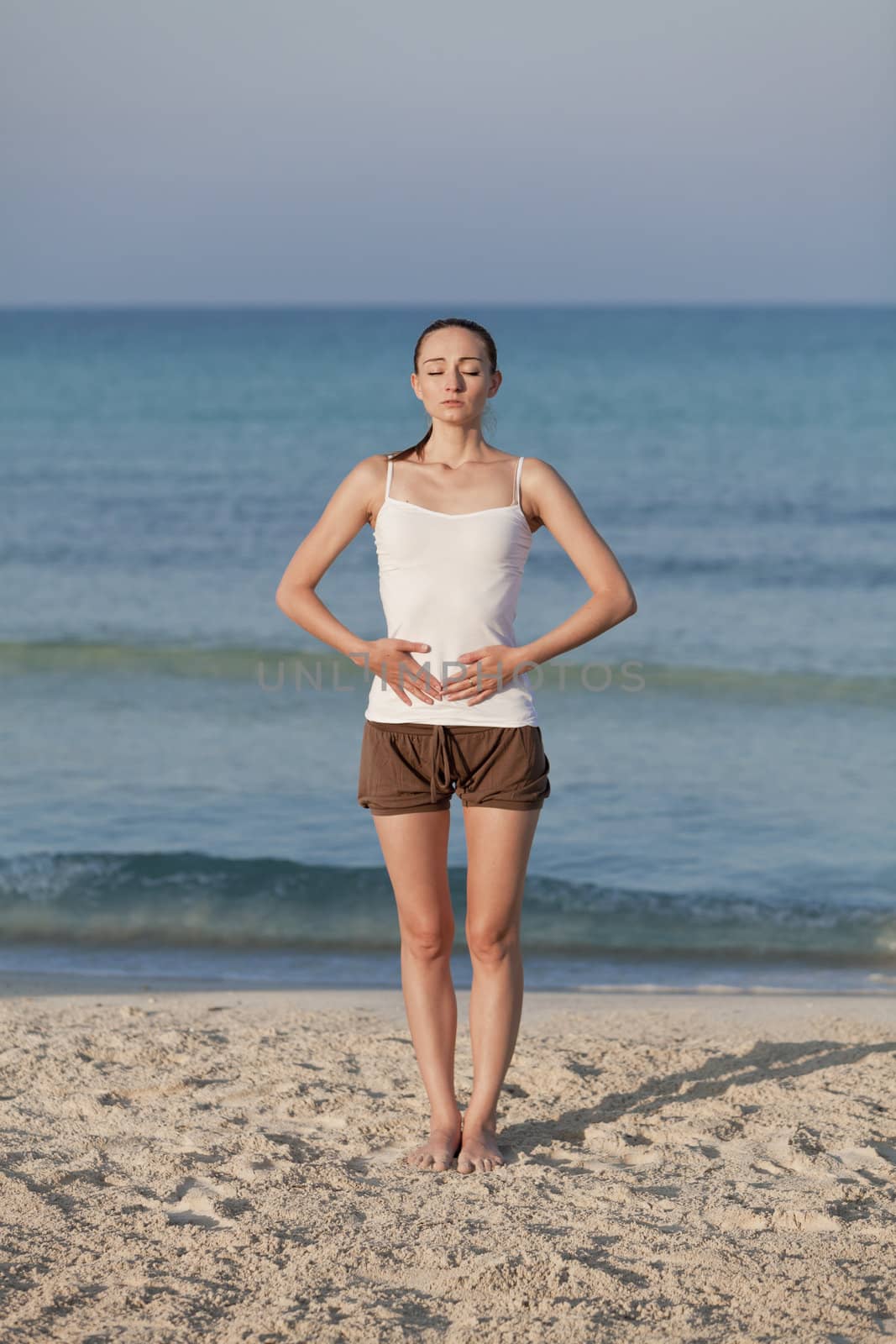 Young sporty woman doing sport yoga on the beach in the sand on the beach in the sun