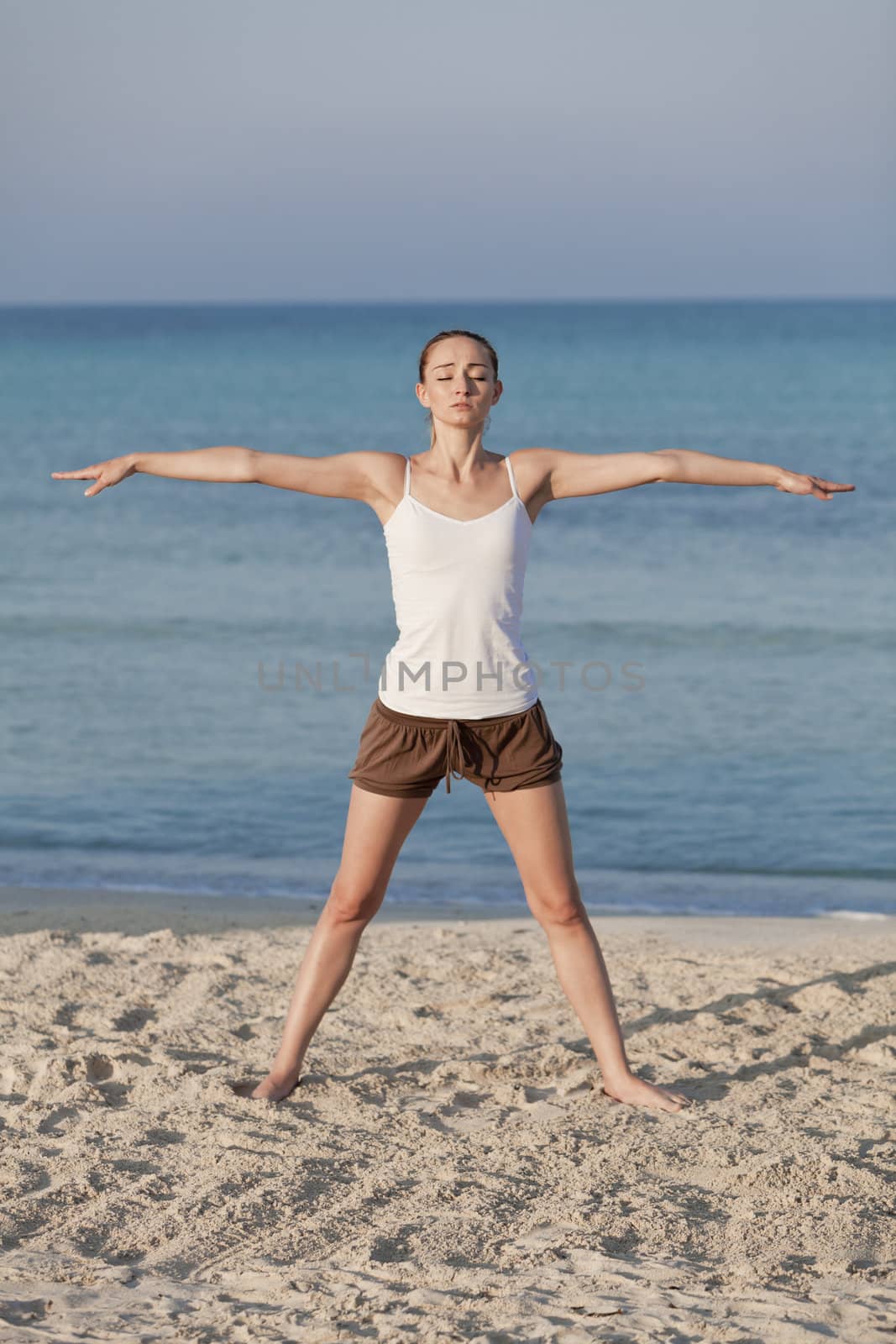 Young sporty woman doing sport yoga on the beach in the sand on the beach in the sun
