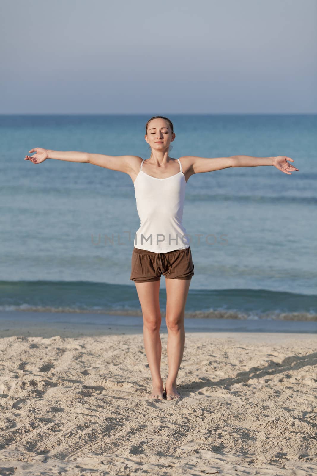 Young sporty woman doing sport yoga on the beach in the sand on the beach in the sun