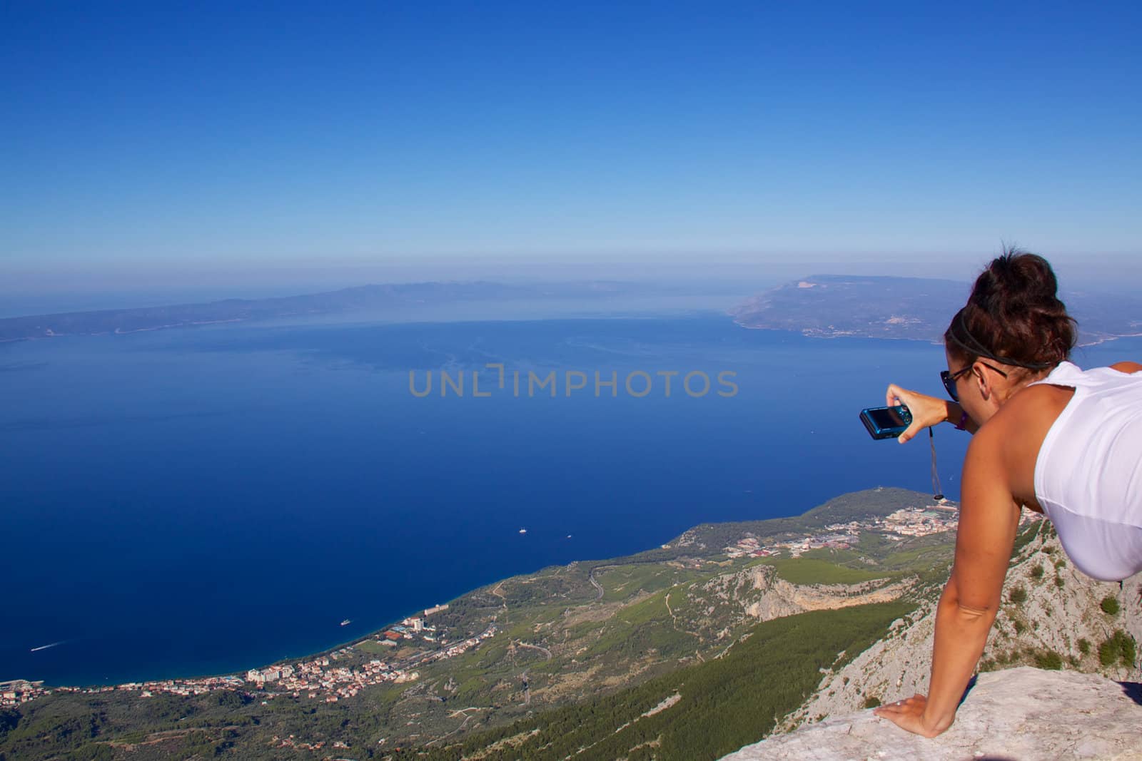 Young girl photographing panoramic view from mountain in picturesque nature park Biokovo on Dalmatian coast near Makarska Riviera in Croatia