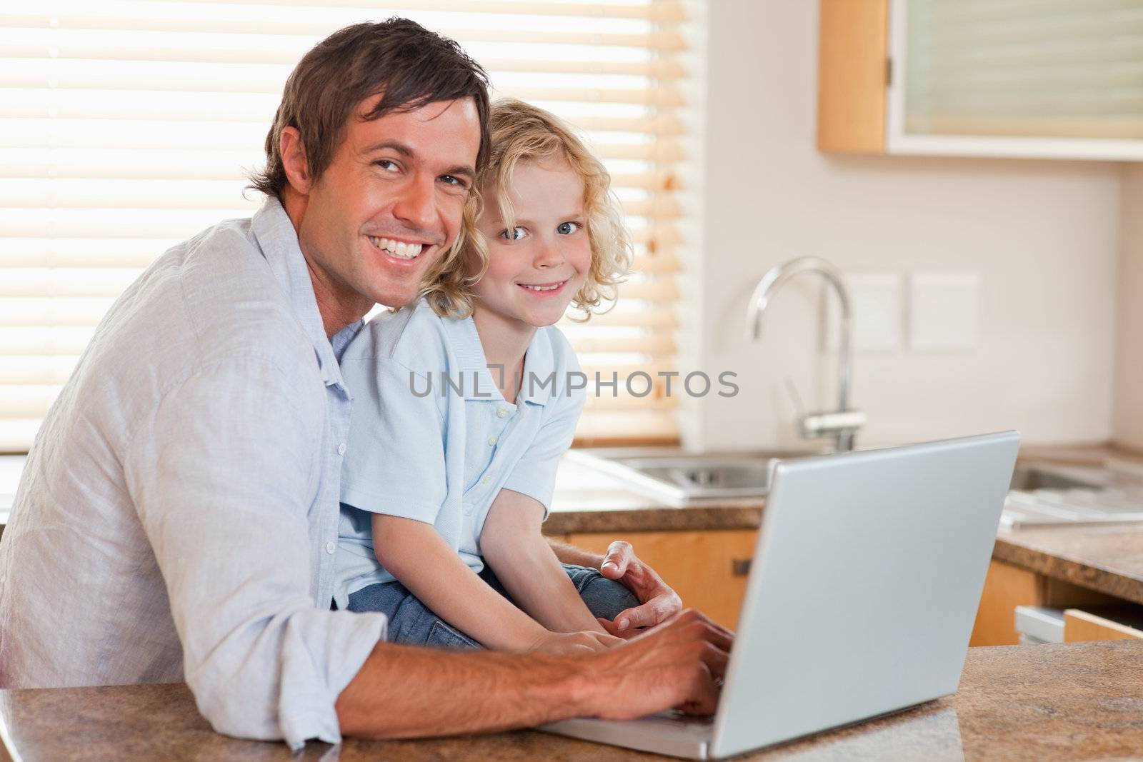 Boy and his father using a notebook together in a kitchen