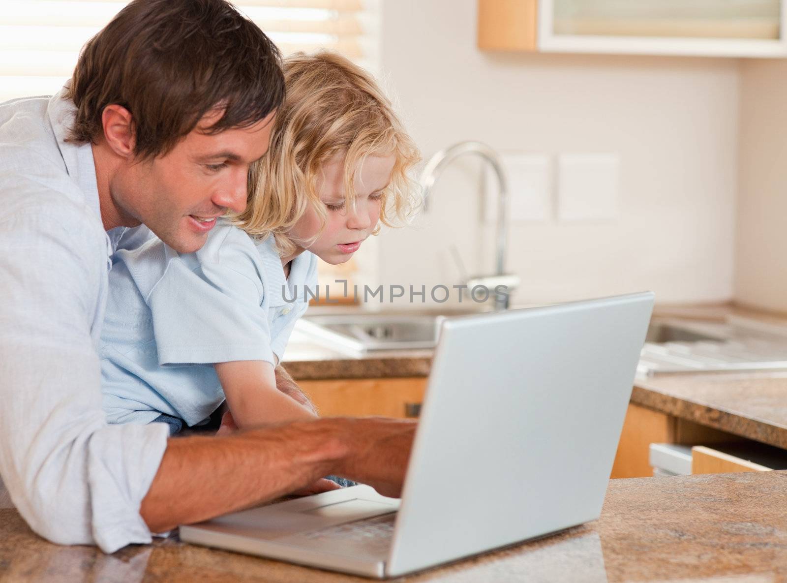 Cute boy and his father using a laptop together in a kitchen