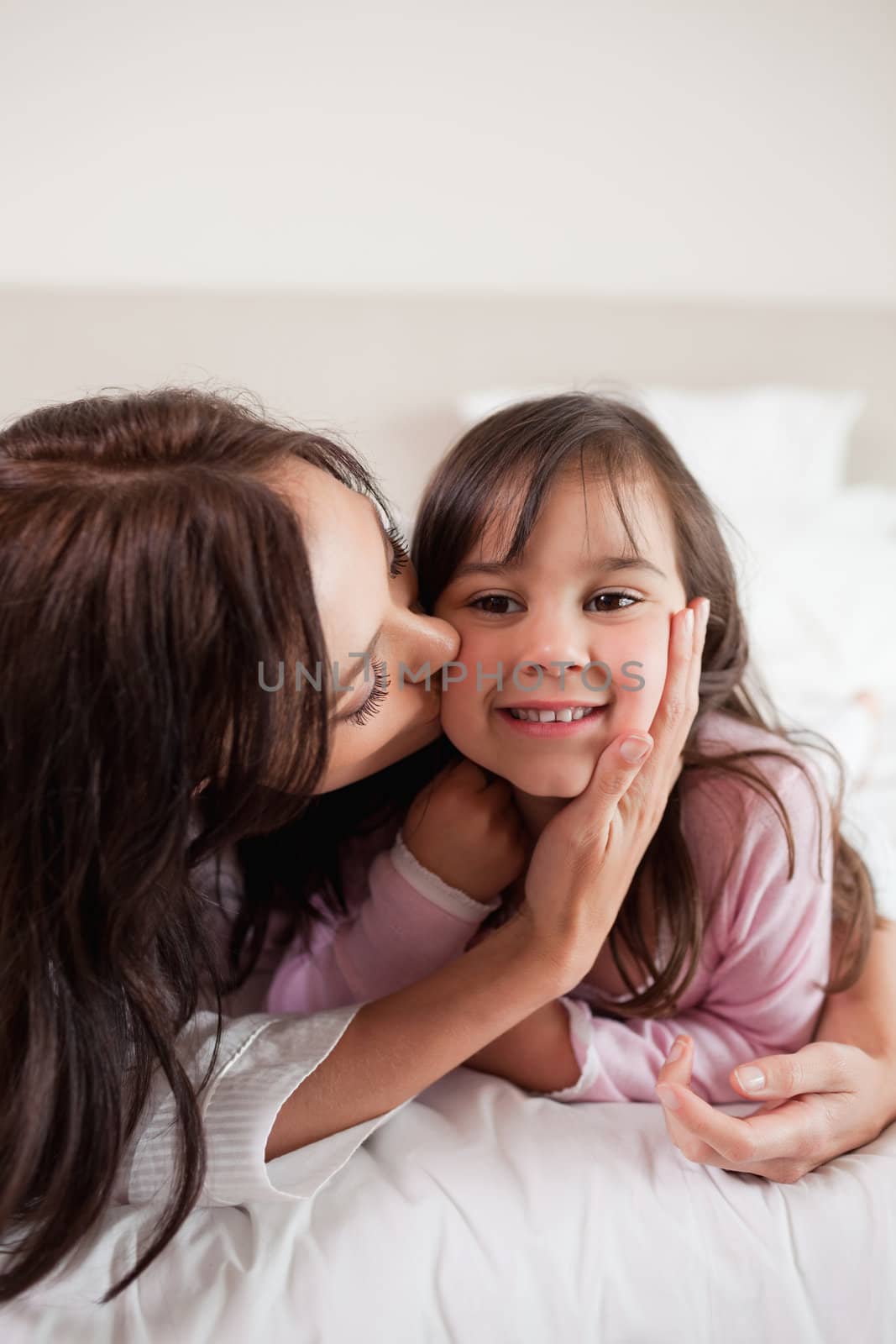 Portrait of a mother kissing her daughter in a bedroom