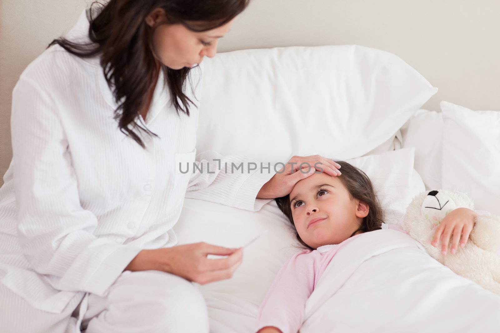Mother checking on her daughter's temperature in a bedroom