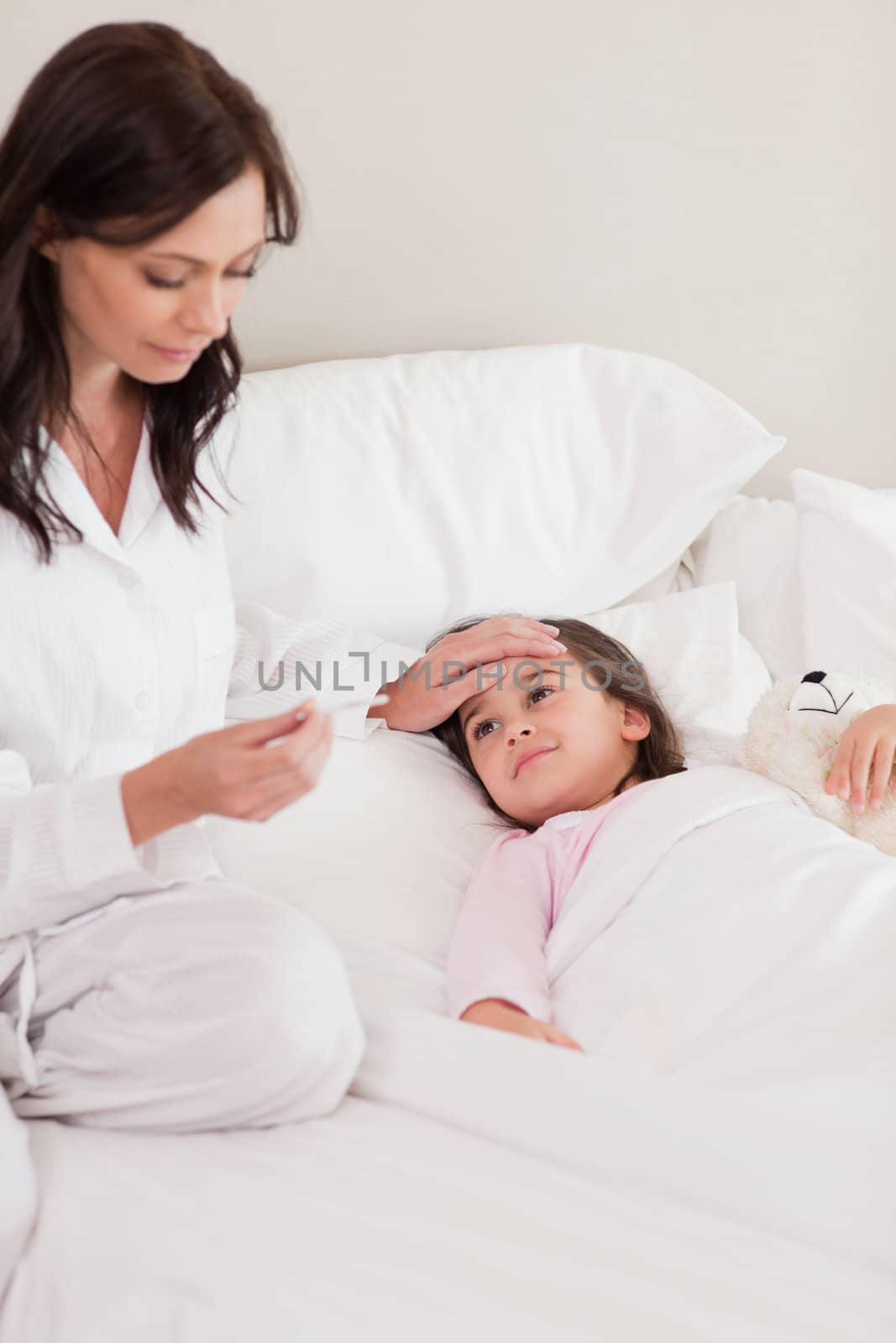 Portrait of a mother checking on her daughter's temperature in a bedroom