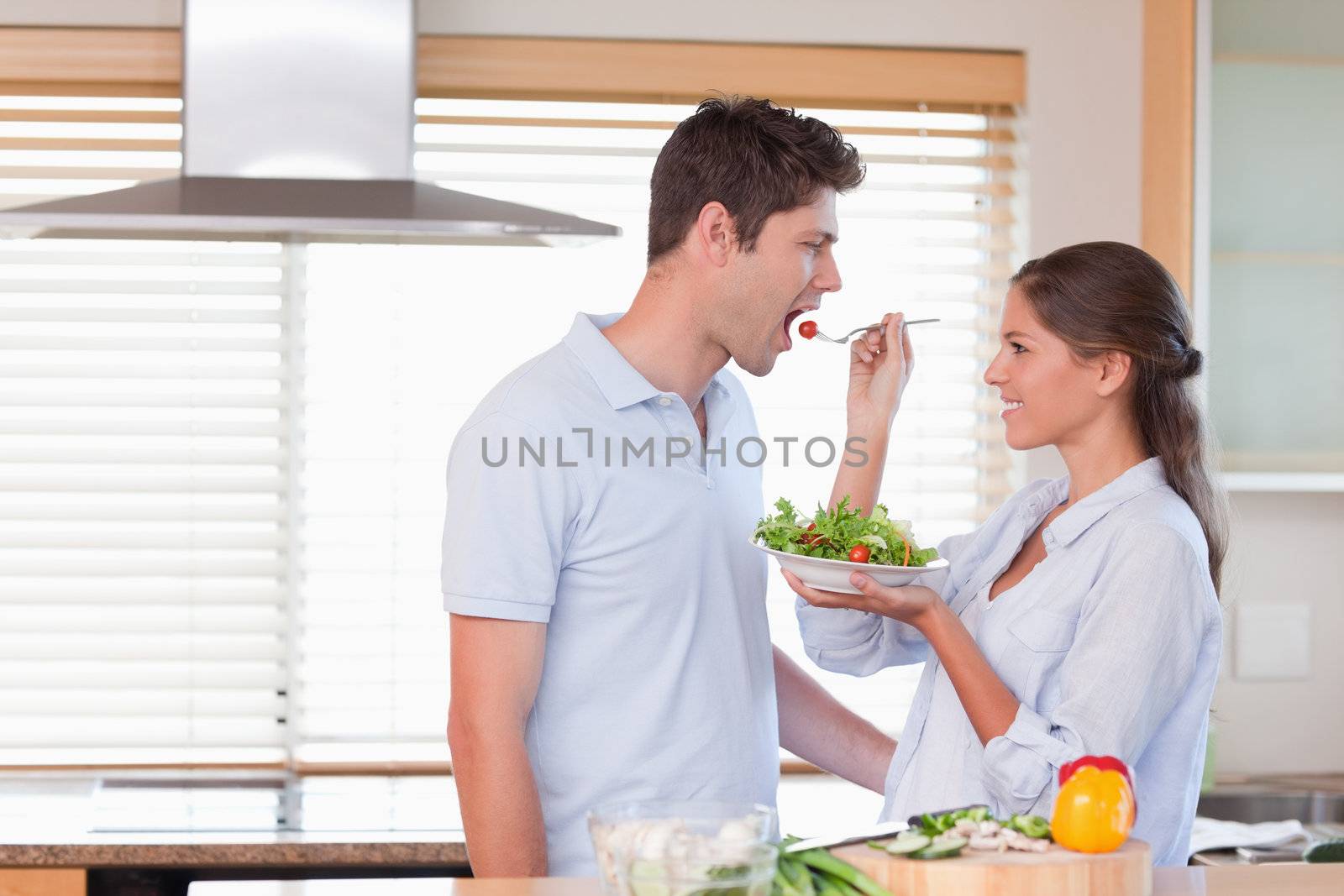 Happy couple tasting a salad in their kitchen