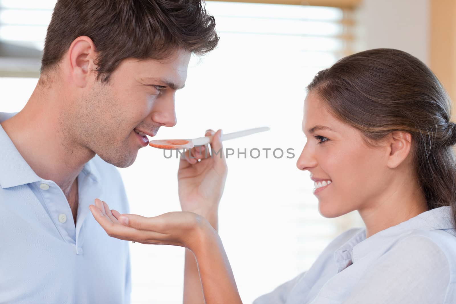 Close up of a man tasting his wife's sauce in their kitchen
