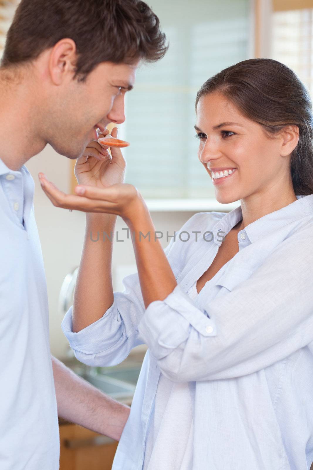 Portrait of a man tasting his wife's sauce in their kitchen