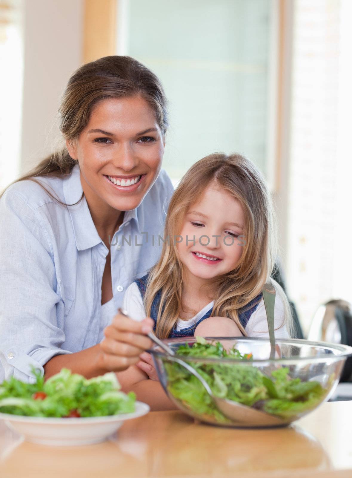 Portrait of a young mother and her daughter preparing a salad in their kitchen