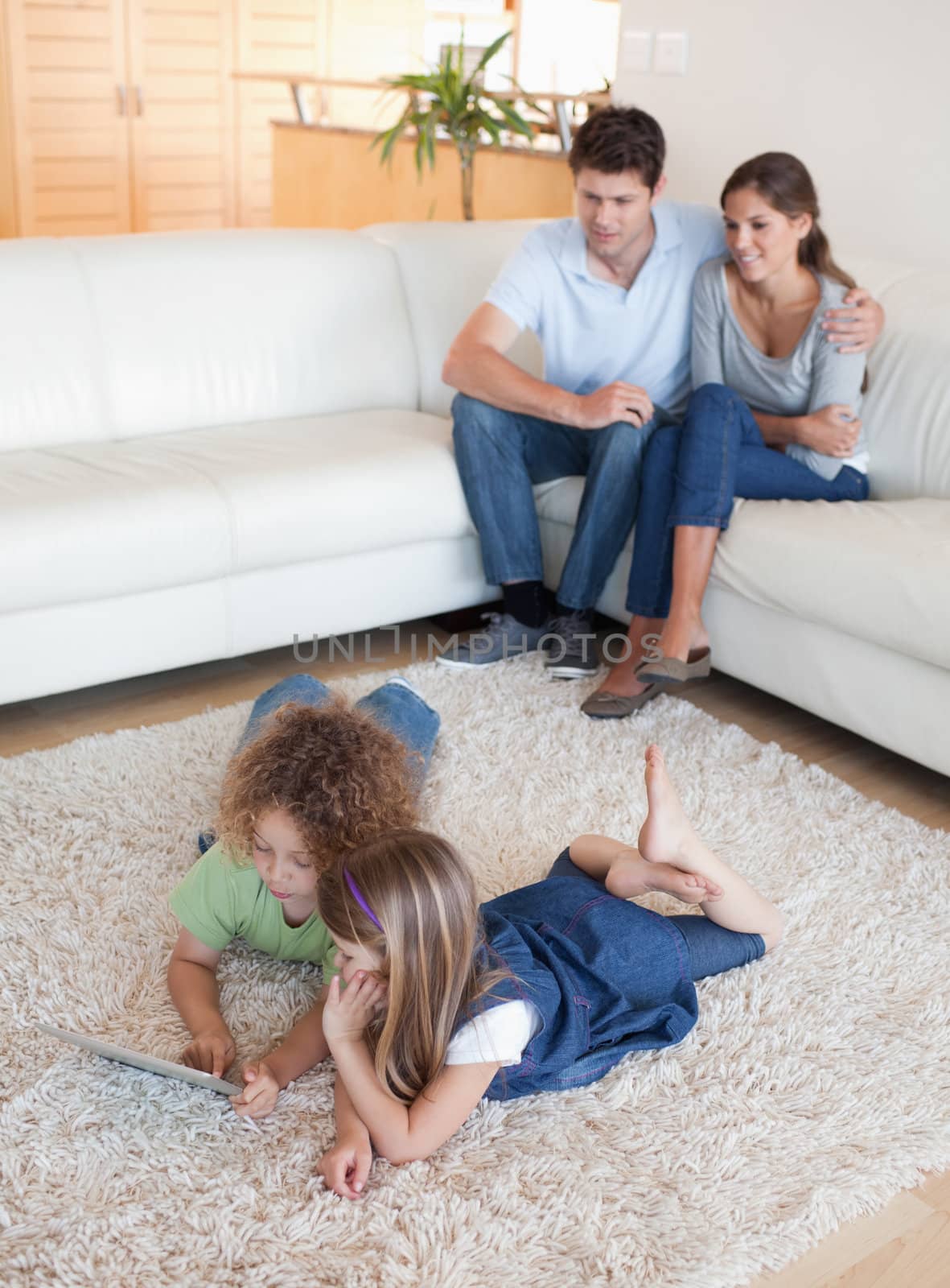 Portrait of children using a tablet computer while their happy parents are watching in their living room