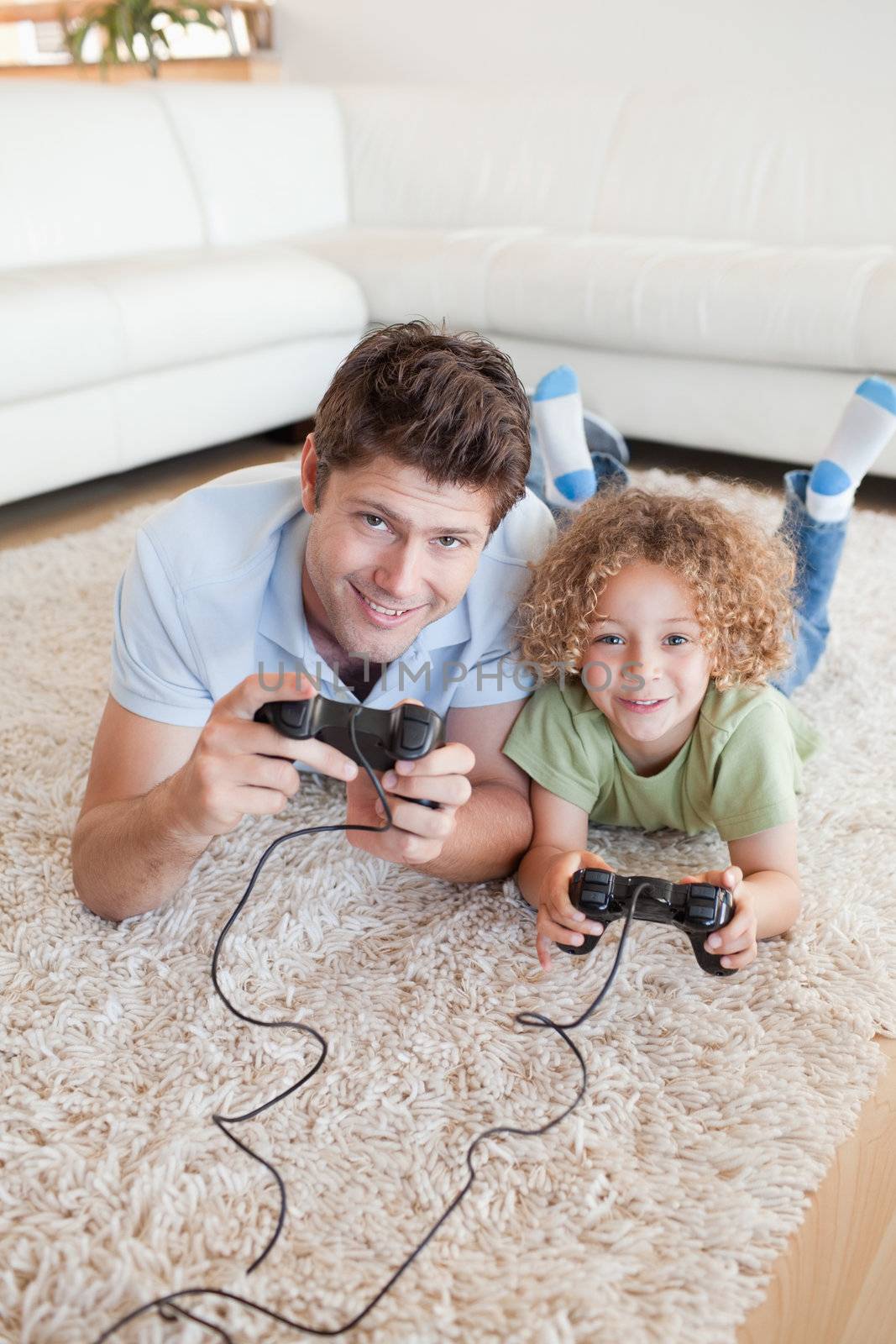 Portrait of a boy and his father playing video games while lying on a carpet
