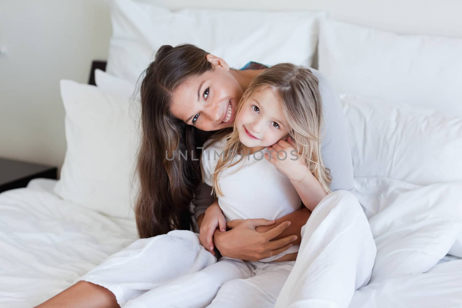 Mother and her daughter posing on a bed while looking at the camera