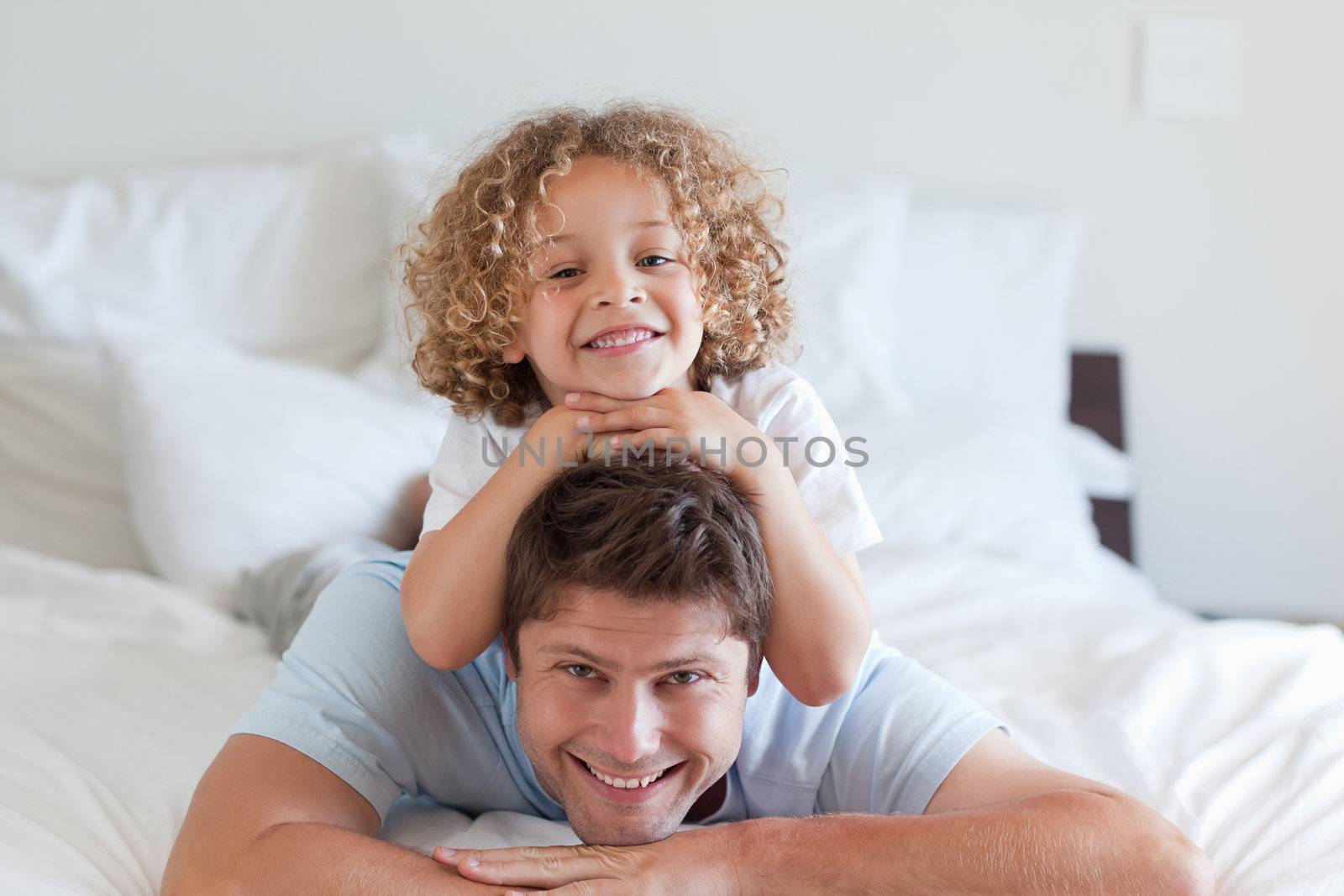 Child lying on fathers back in bed