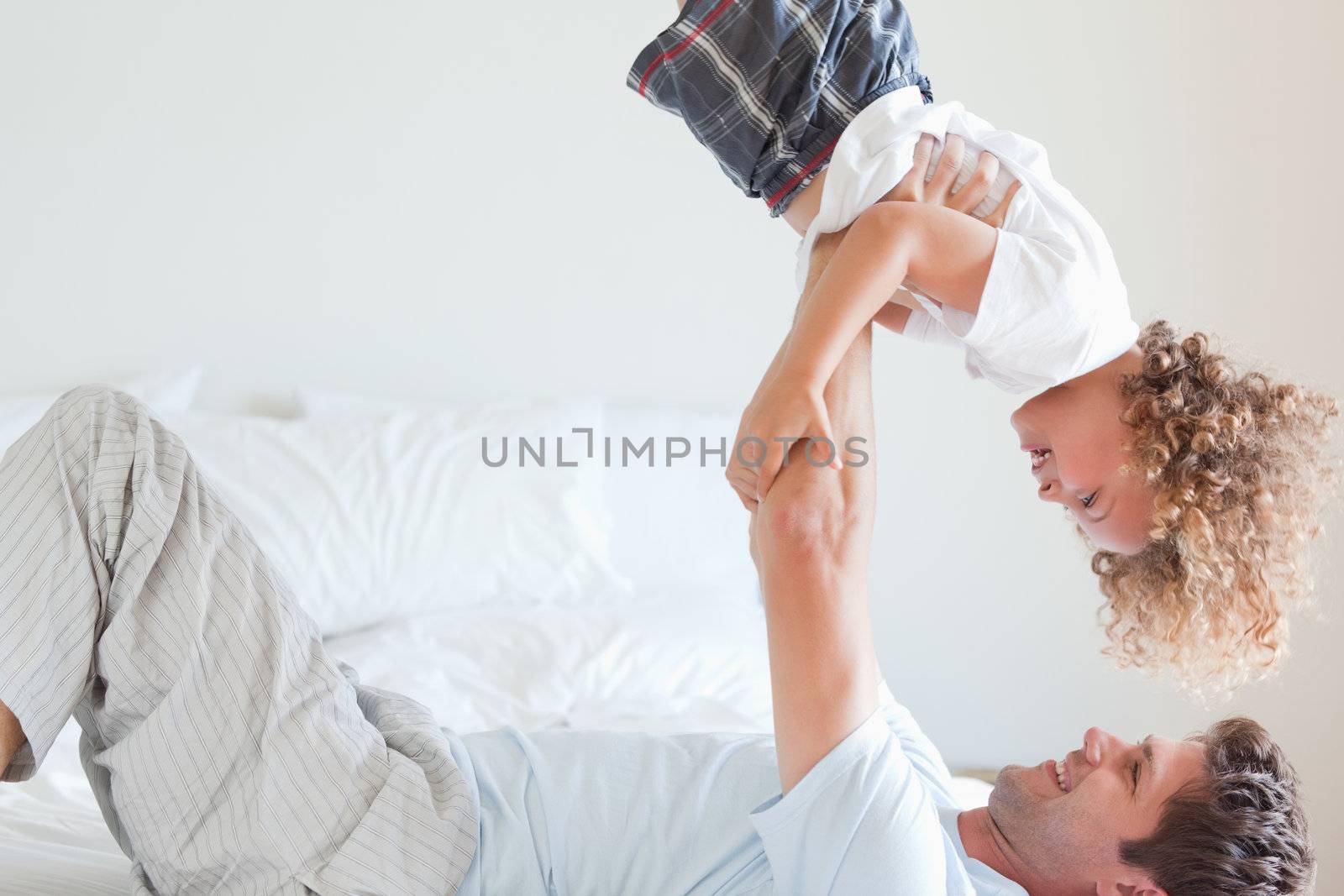 Side view of father lifting smiling child on bed