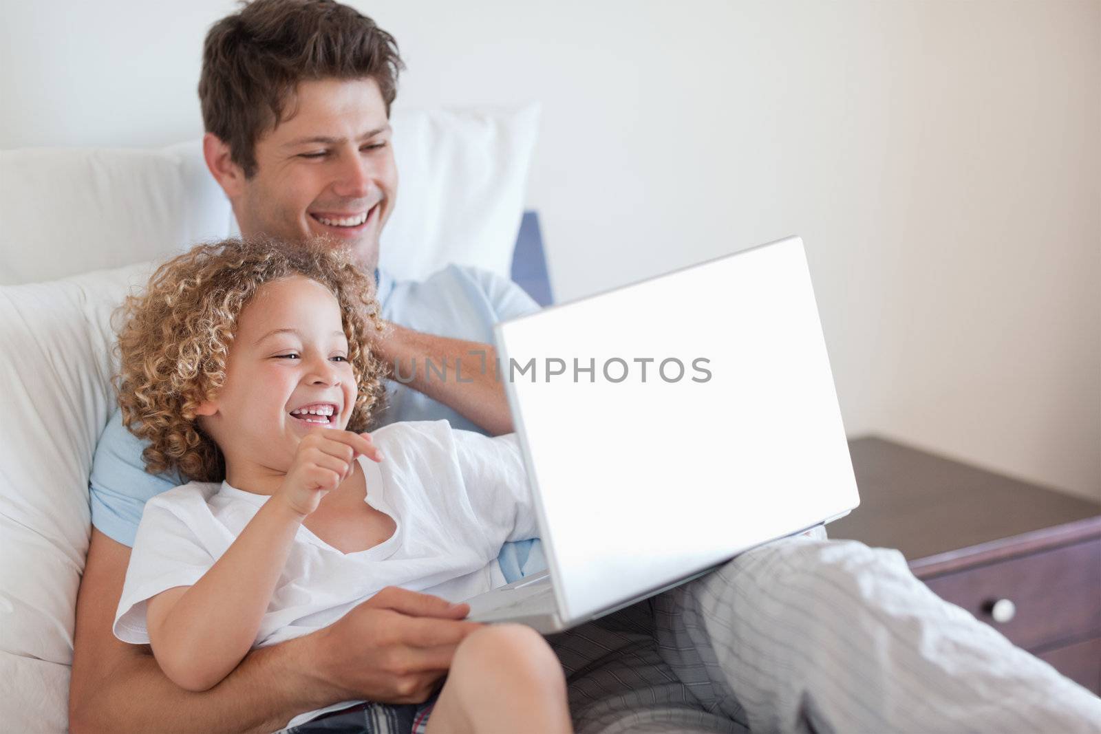 Father and child using laptop together in bed
