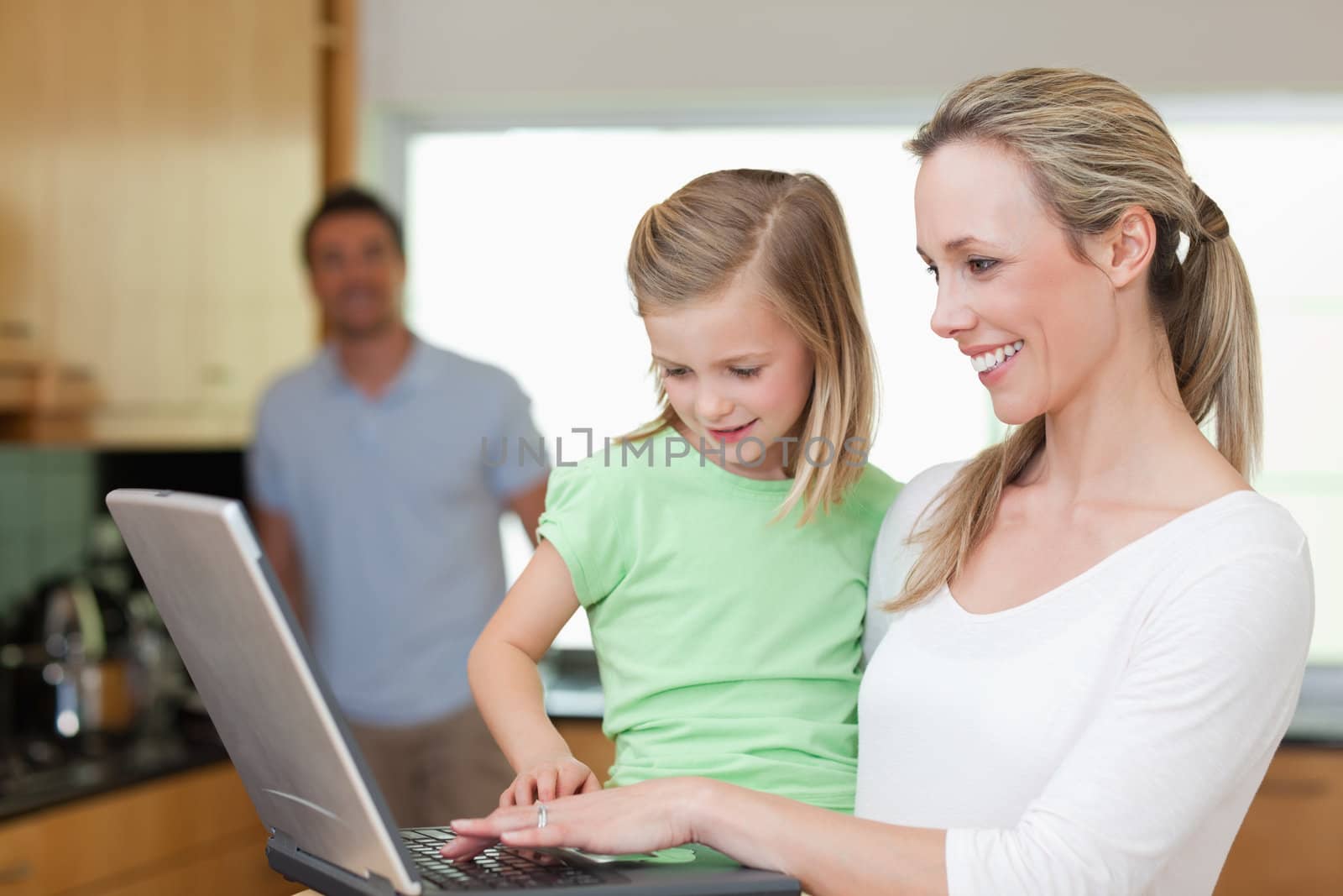 Happy mother and daughter surfing the web together with father in the background