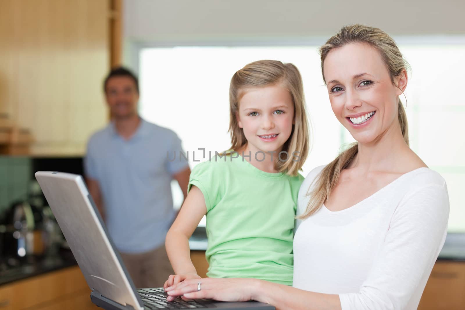 Mother and daughter using laptop together with father in the background